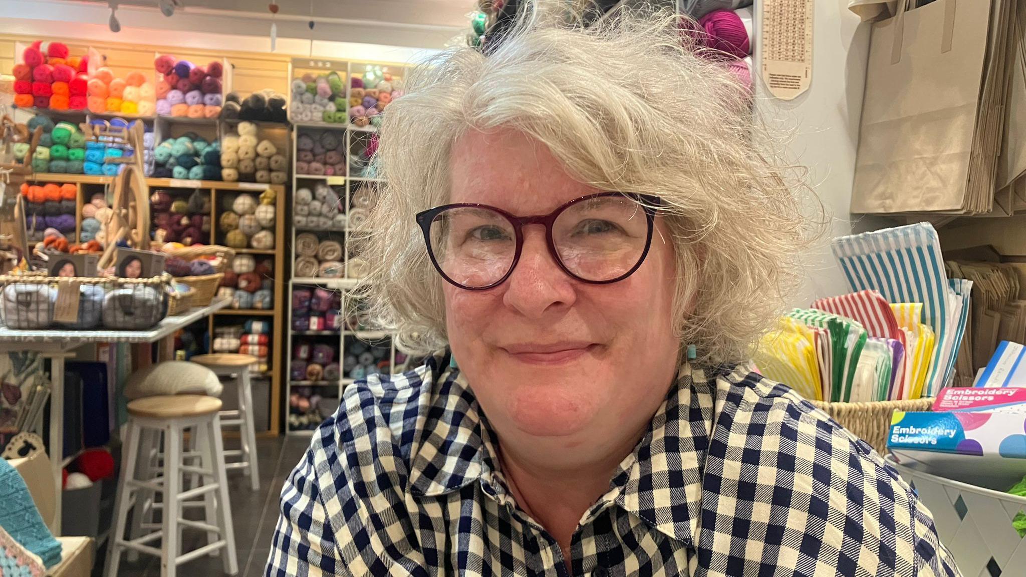 Katie Raynor, owner of Crafty Praxis Yarns, smiling in her store with colourful yarns behind her