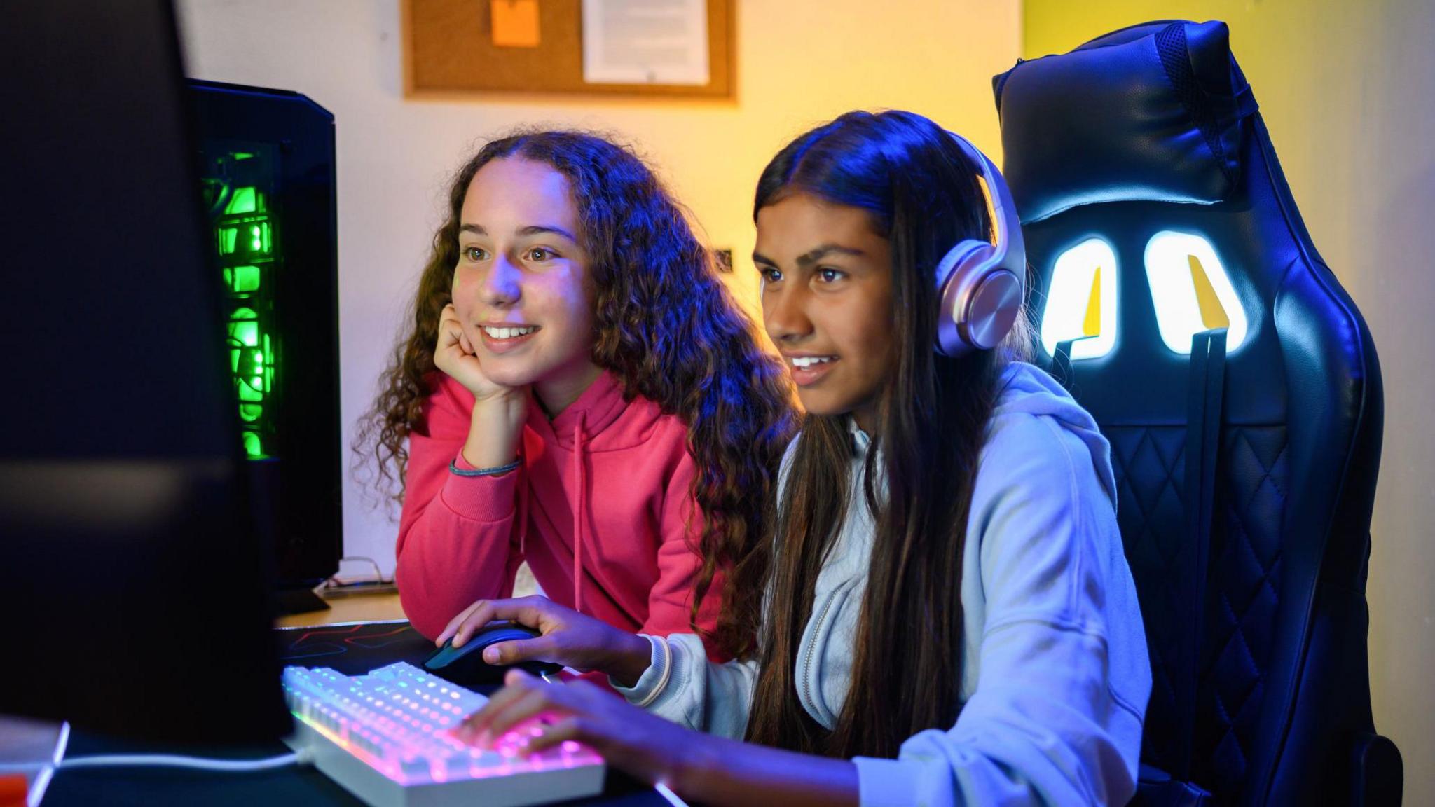 Teens looking at screen of monitor while sitting at table with gaming PC and using keyboard to play game in room.