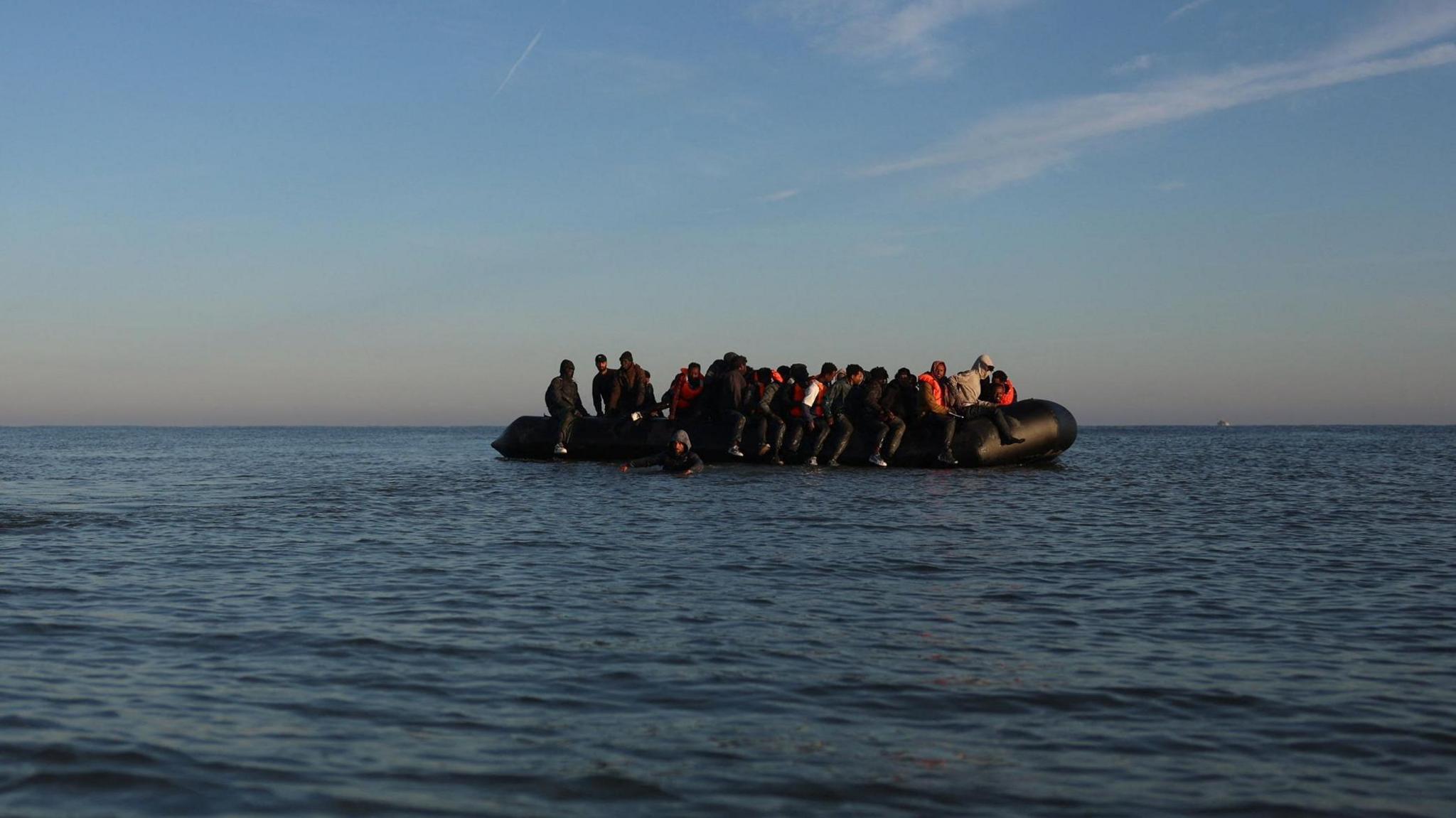 Black inflatable dinghy in the English Channel. It is filled with people.