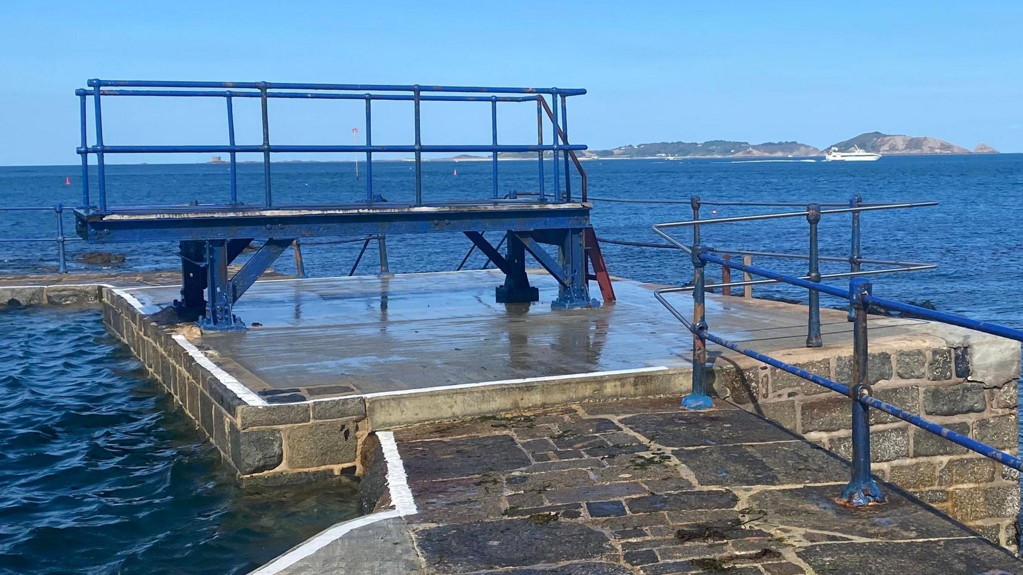 The diving board is pictured at high tide against a blue sky with Herm in the background.
