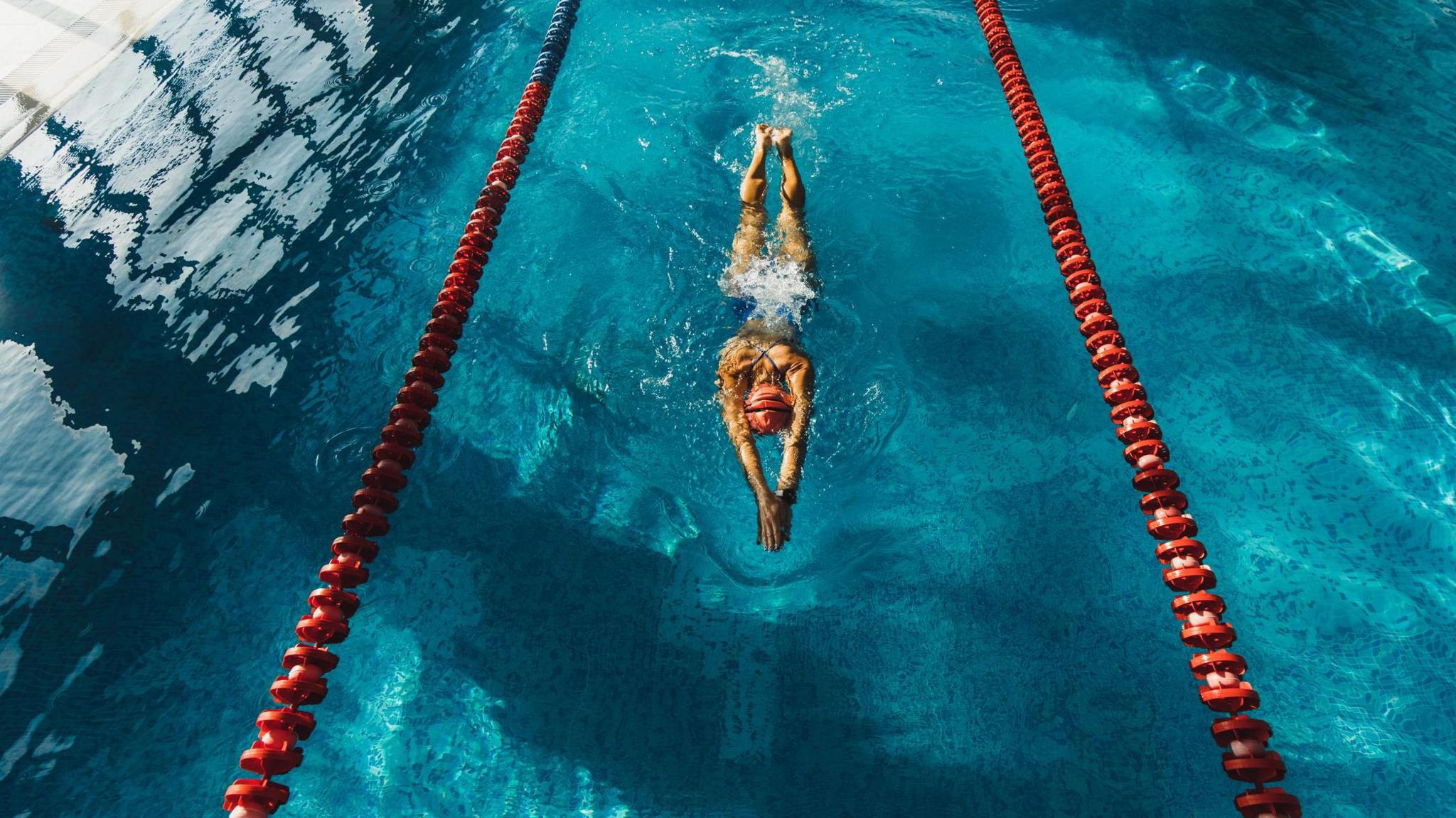 A woman swimming between two lane ropes with a clear blue water surface.