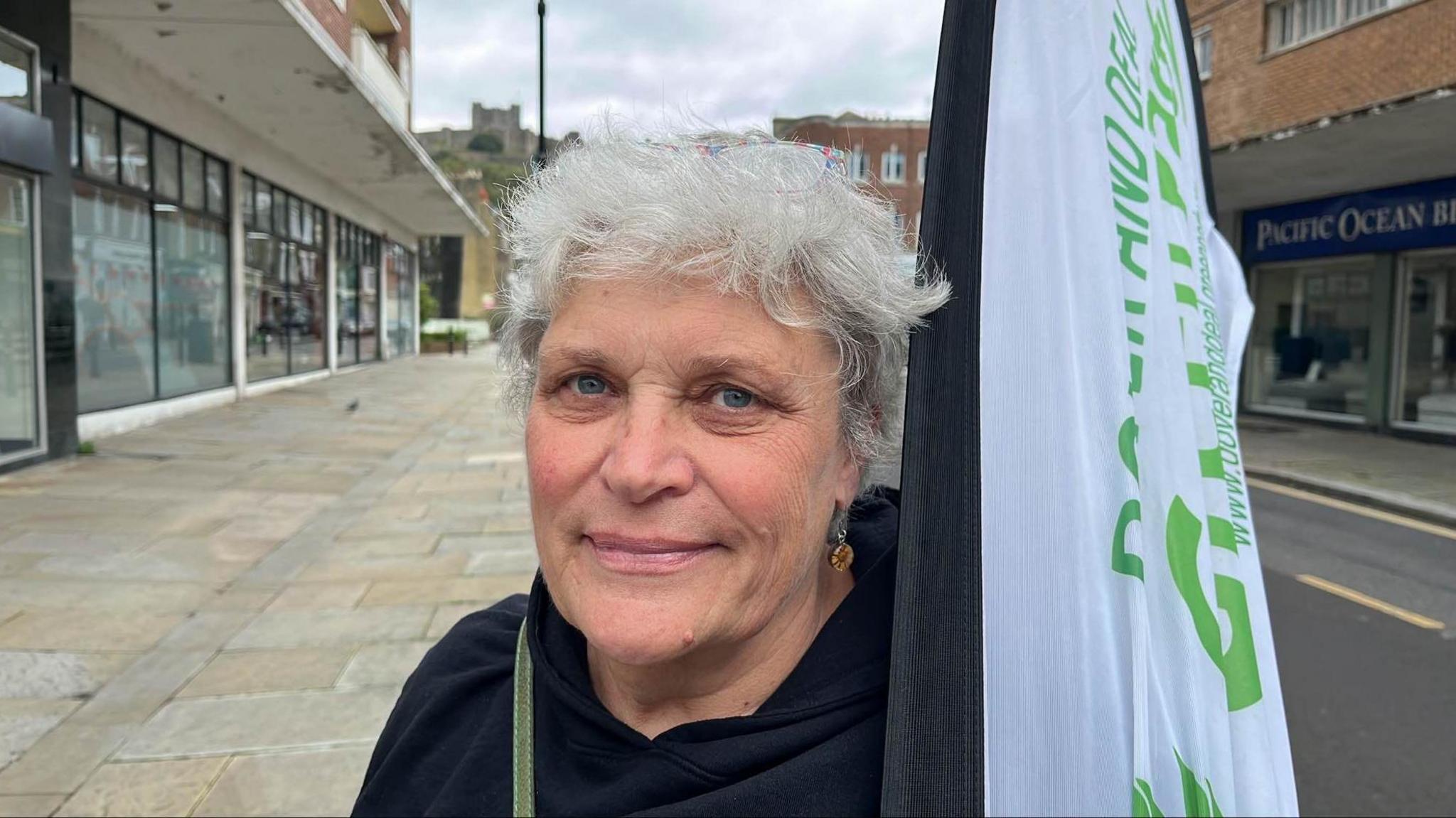 Sarah Waite from the Dover and Deal Green Party standing in Dover town centre holding a party flag.