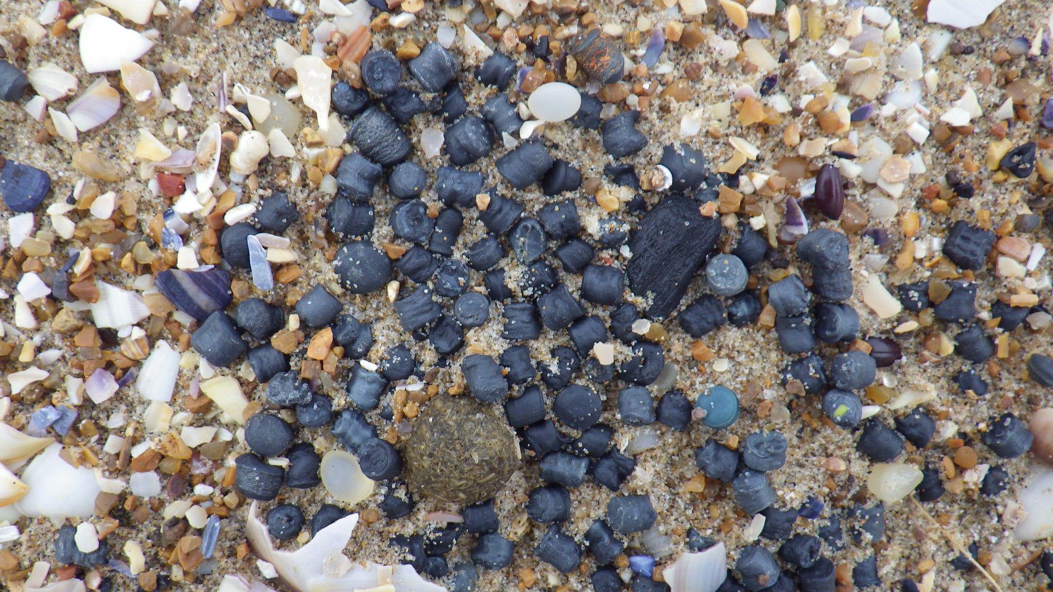 Close up image of lots of black plastic pellet on a beach.