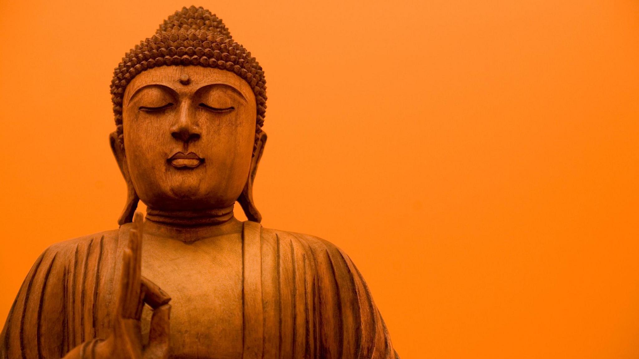 A wooden carving of Buddha on an orange background.