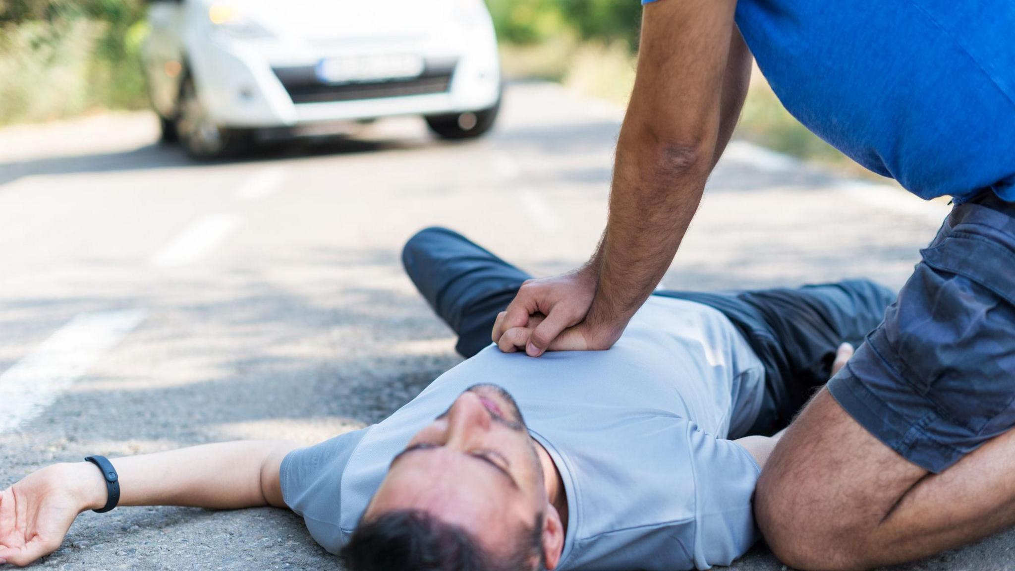 A driver is giving a man CPR chest compressions at the roadside.