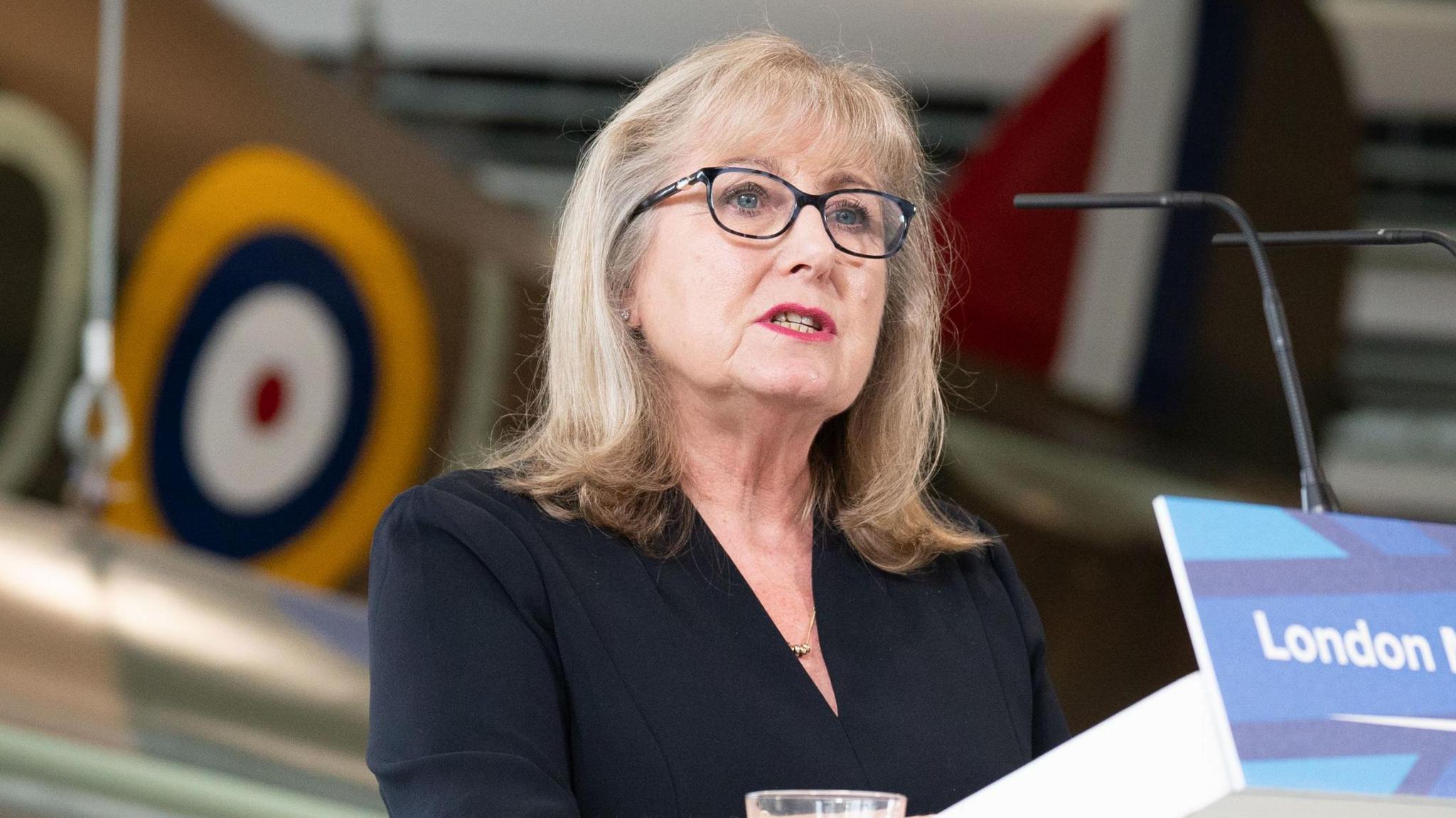 Susan Hall e veshur me një fustan të zi qëndron në një podium