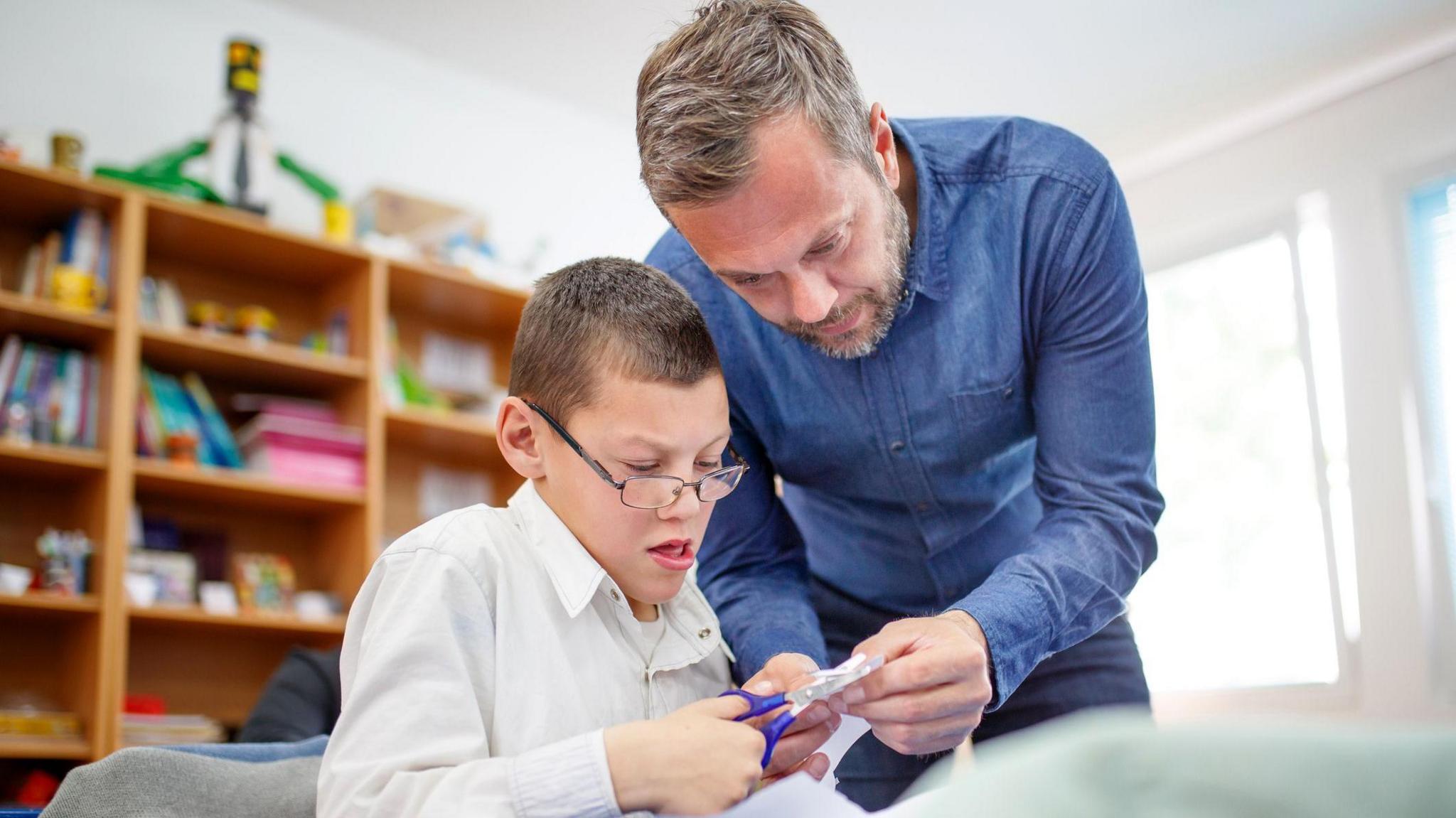 Male teacher helping student using scissors.