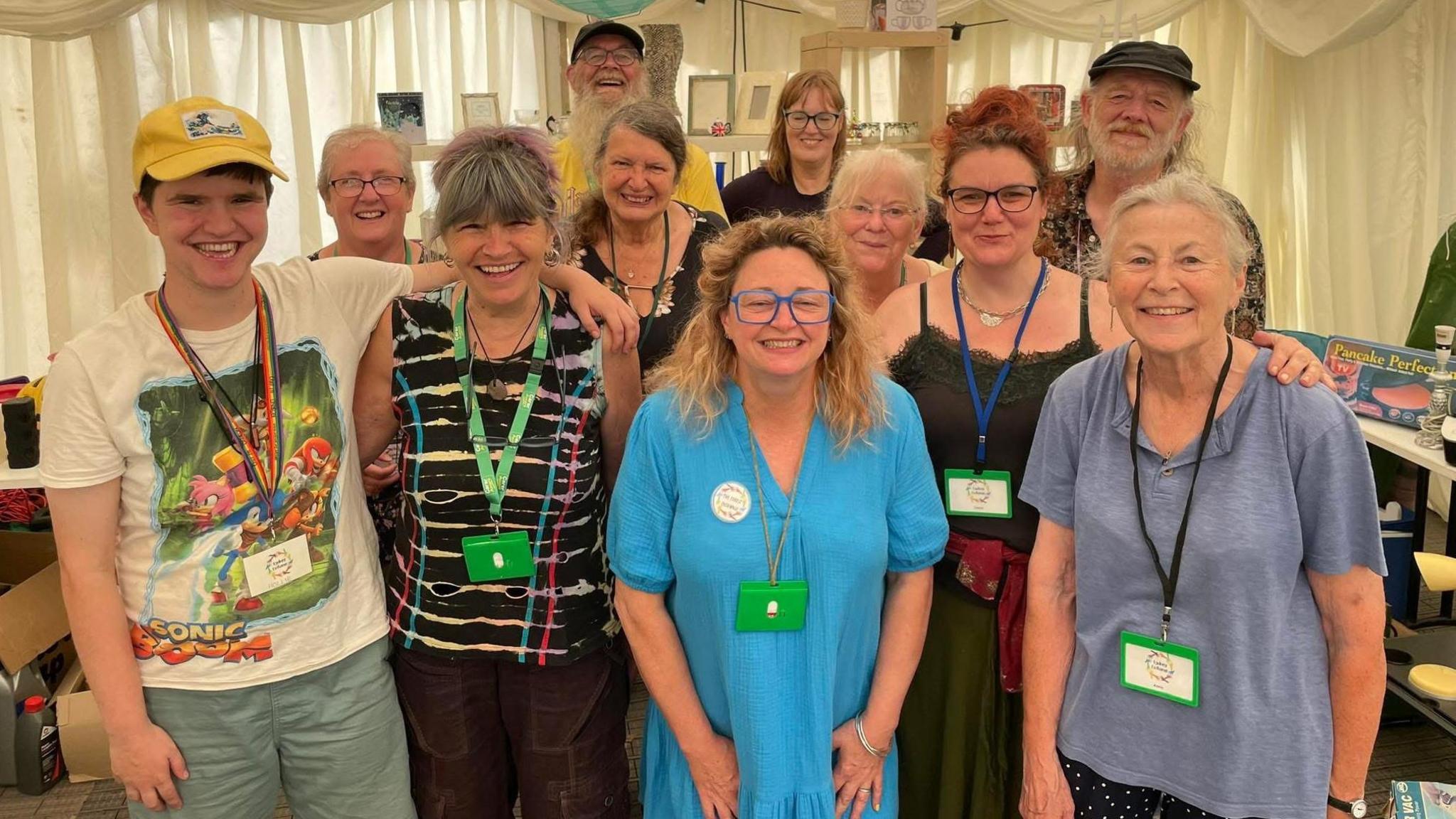 The Forest Exchange team are huddled together in a group picture and are smiling at the camera in a community hall. They are a mixture of men and women.