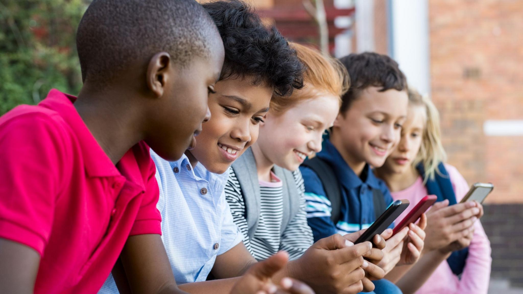 A line of five children looking at their phones