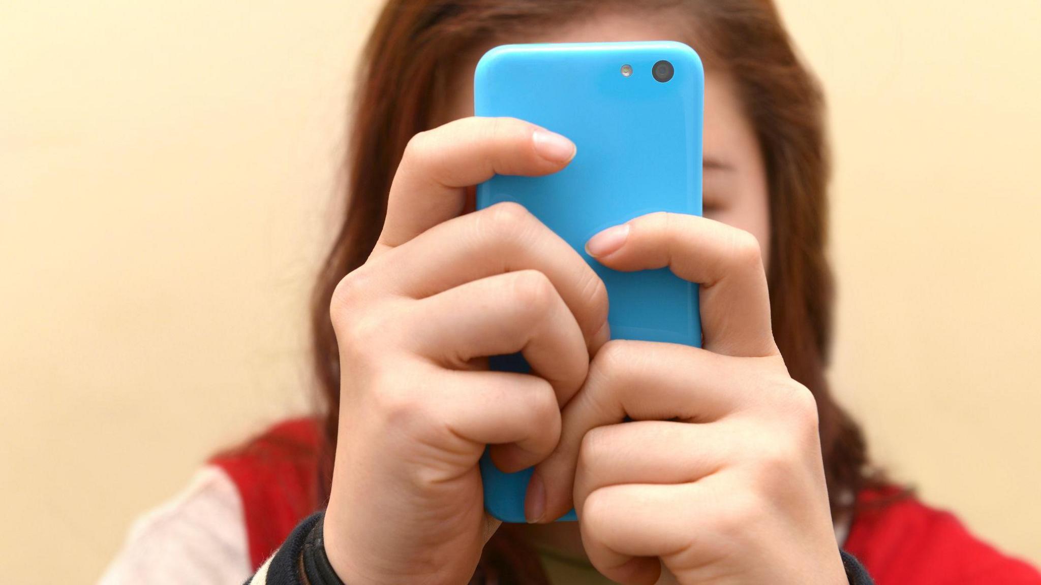 A girl sits with a blue phone in front of her face