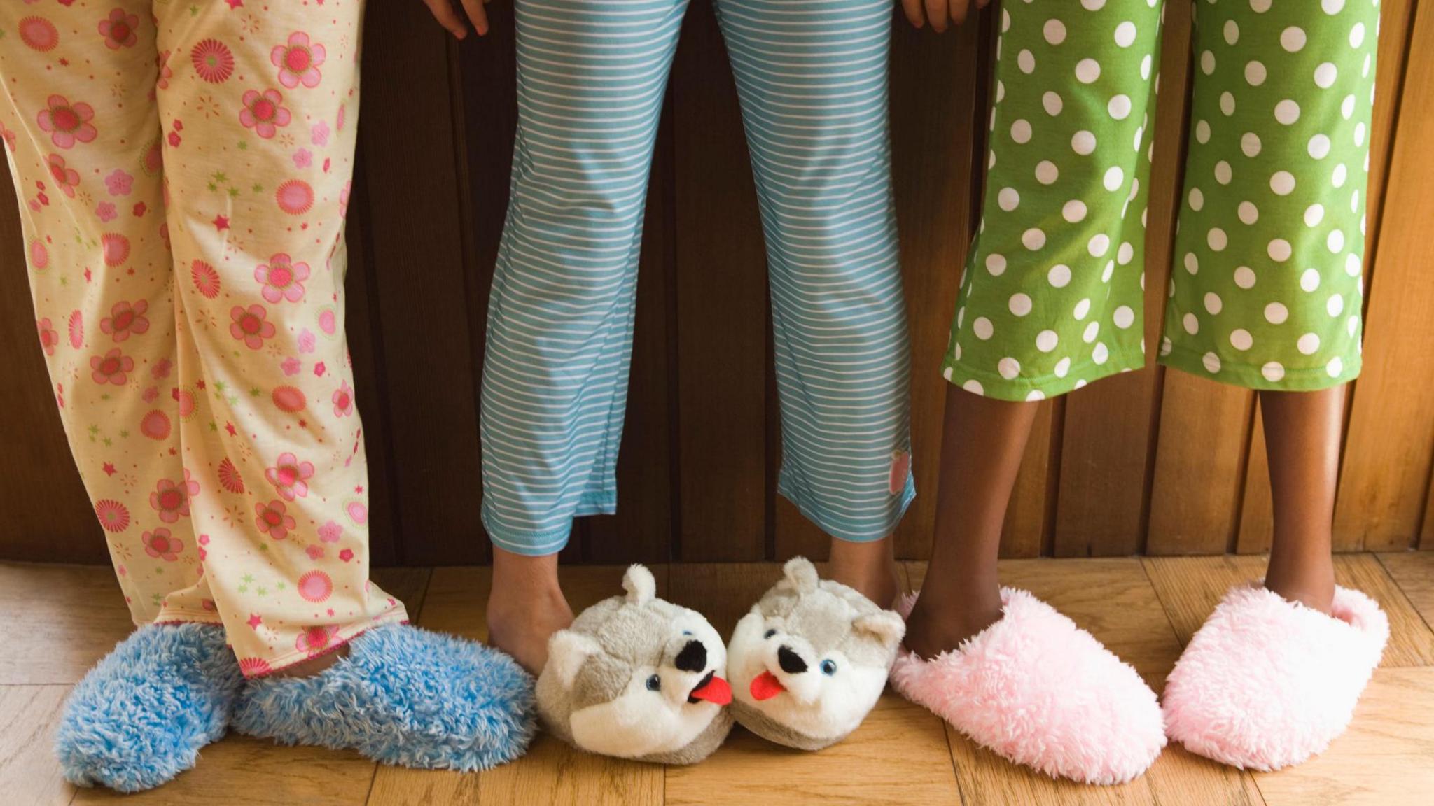 Three pairs of children's legs wearing pyjamas and slippers