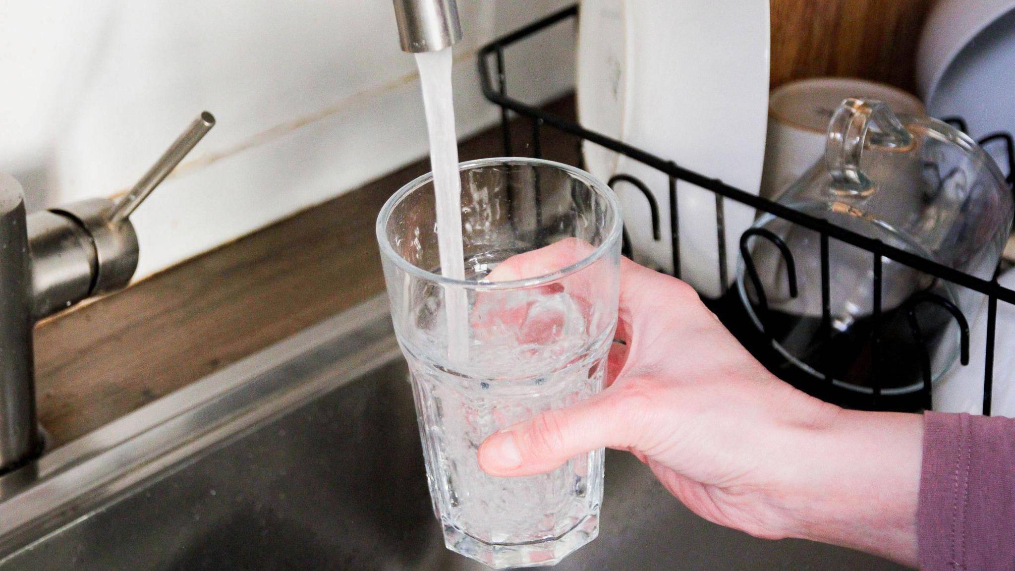 A hand fills a glass of water under a kitchen tap.