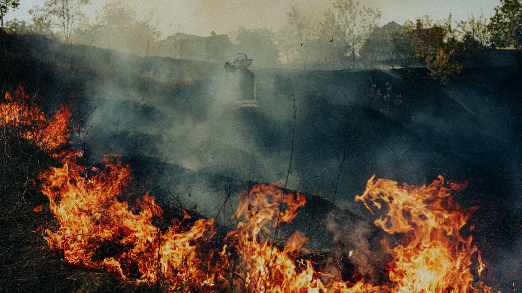 Flames rip through a crater. A firefighter can be seen through the smoke.