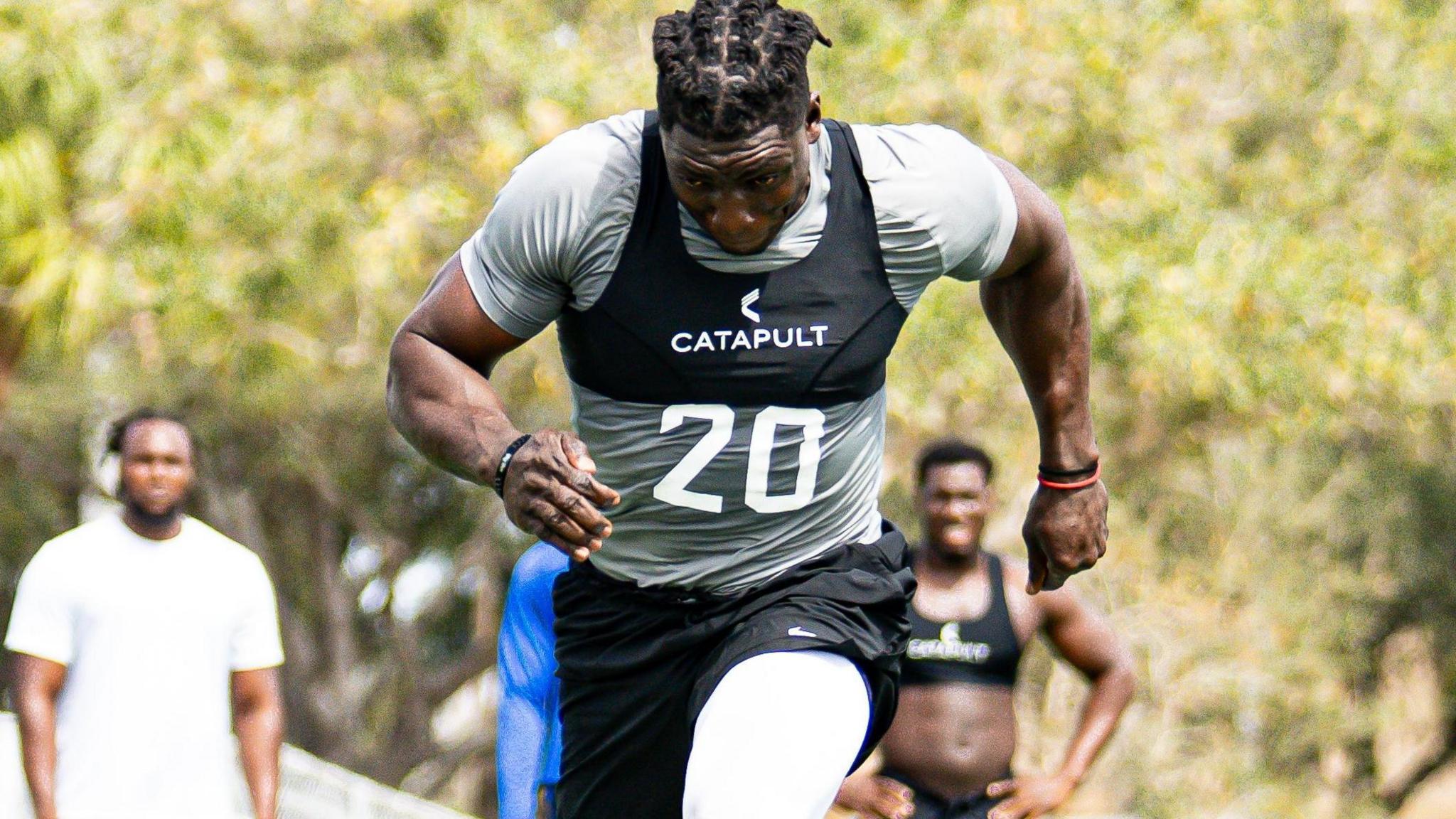 Uar Bernard, wearing black shorts and a black support vest over a grey t-shirt, is seen with his head down while sprinting forward. Out the distance
