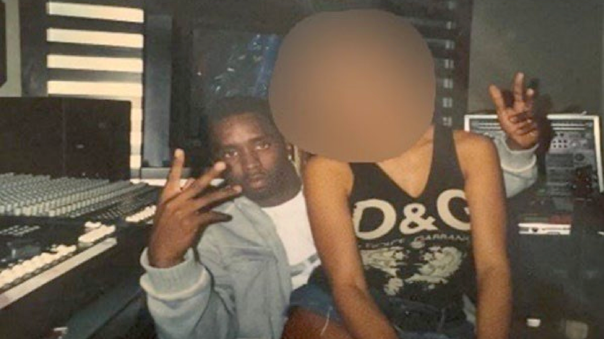 An old colour photograph scanned from a court filing, which appears to show Sean Combs in his studio next to the mixing board, gesturing with both hands at the camera, with a young woman sitting on his lap. The woman's face is blurred out.