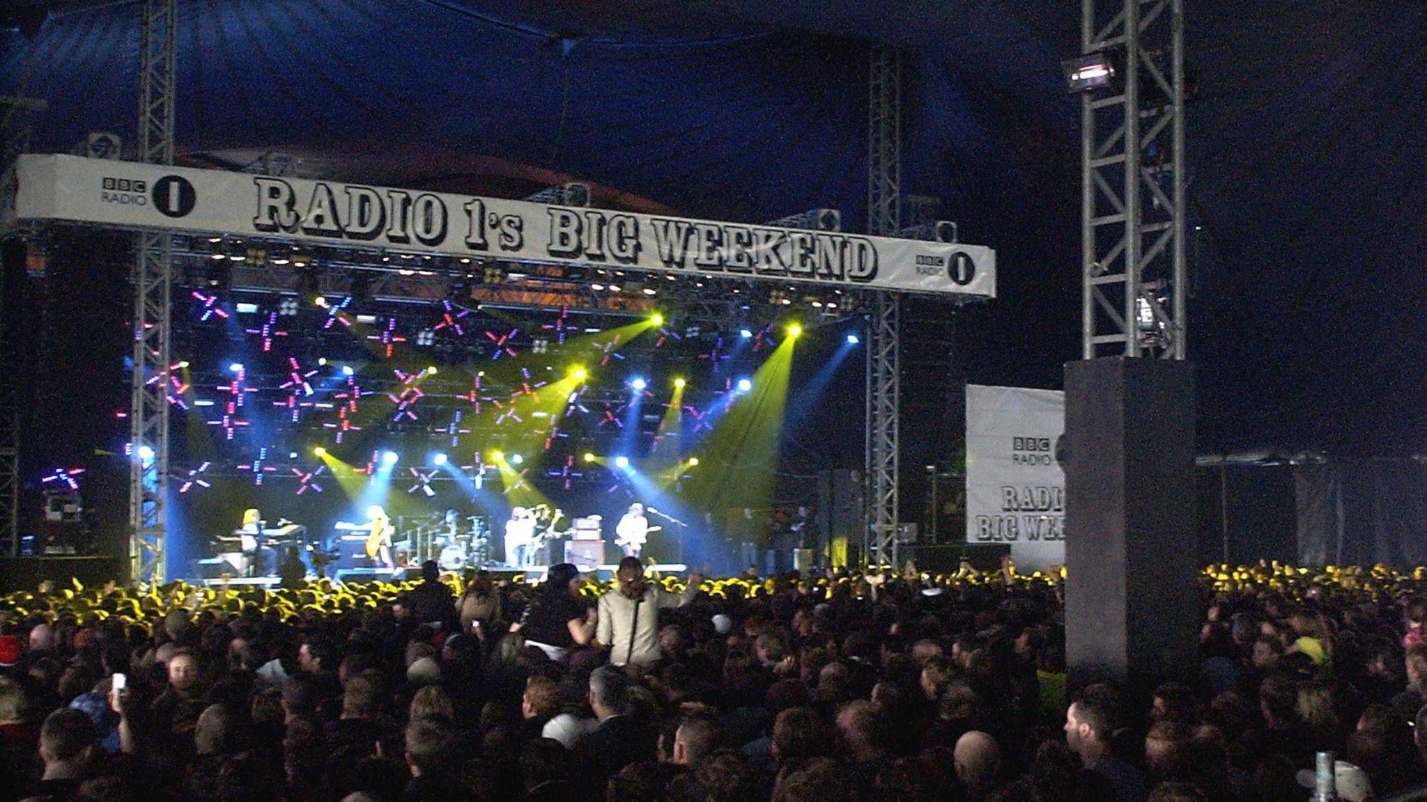 A large crowd of people inside a giant blue marquee looks at a stage, with Radio's Big Weekend branding around it.