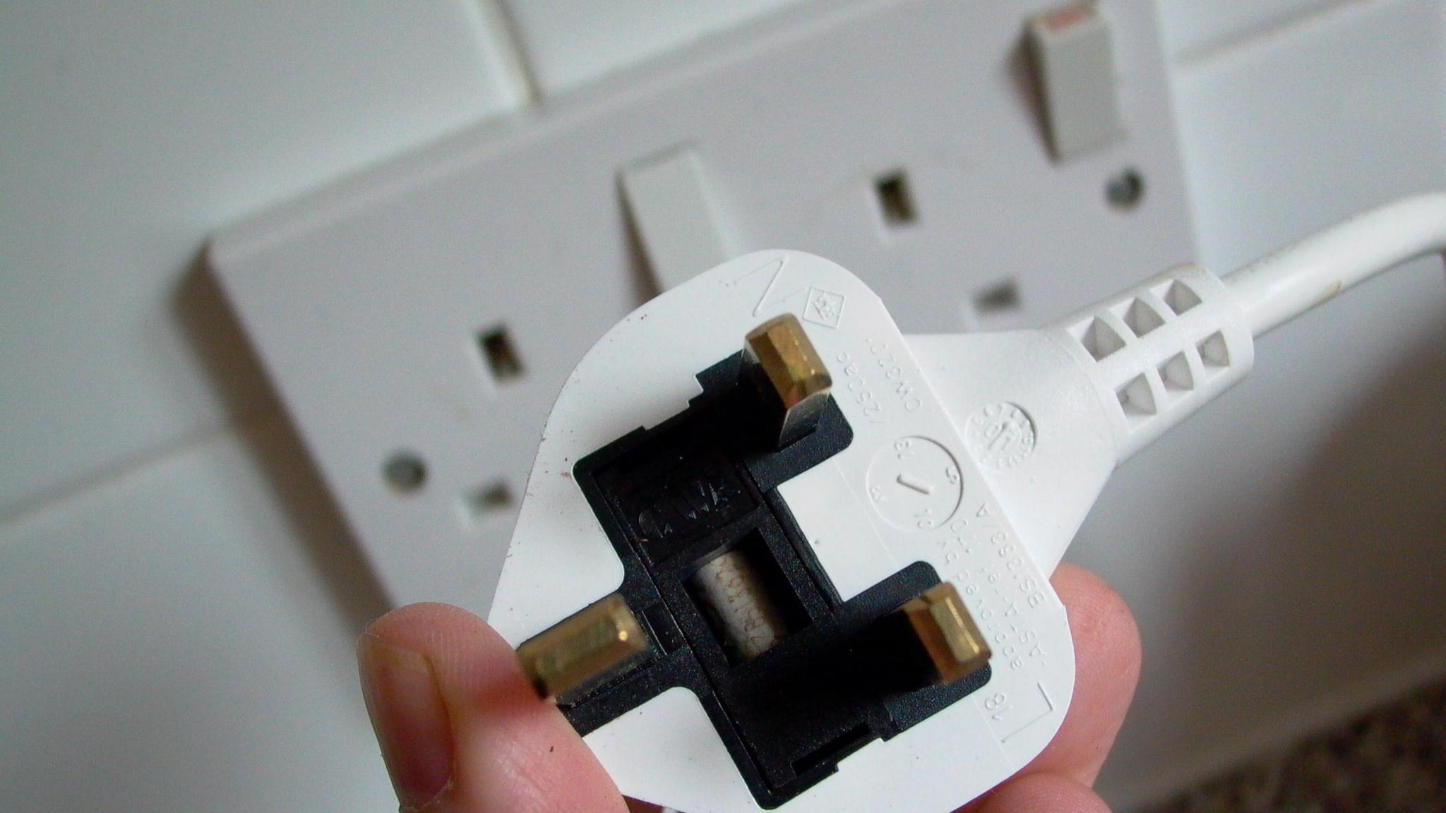 A picture of someone holding a white plug in front of a white power socket