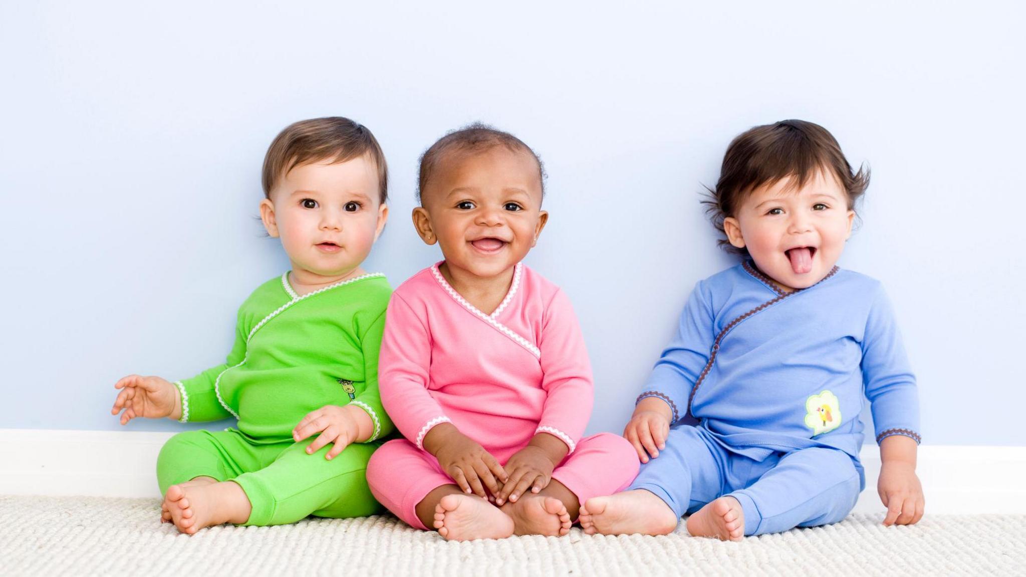 Three young children sitting in pyjamas smiling at the camera