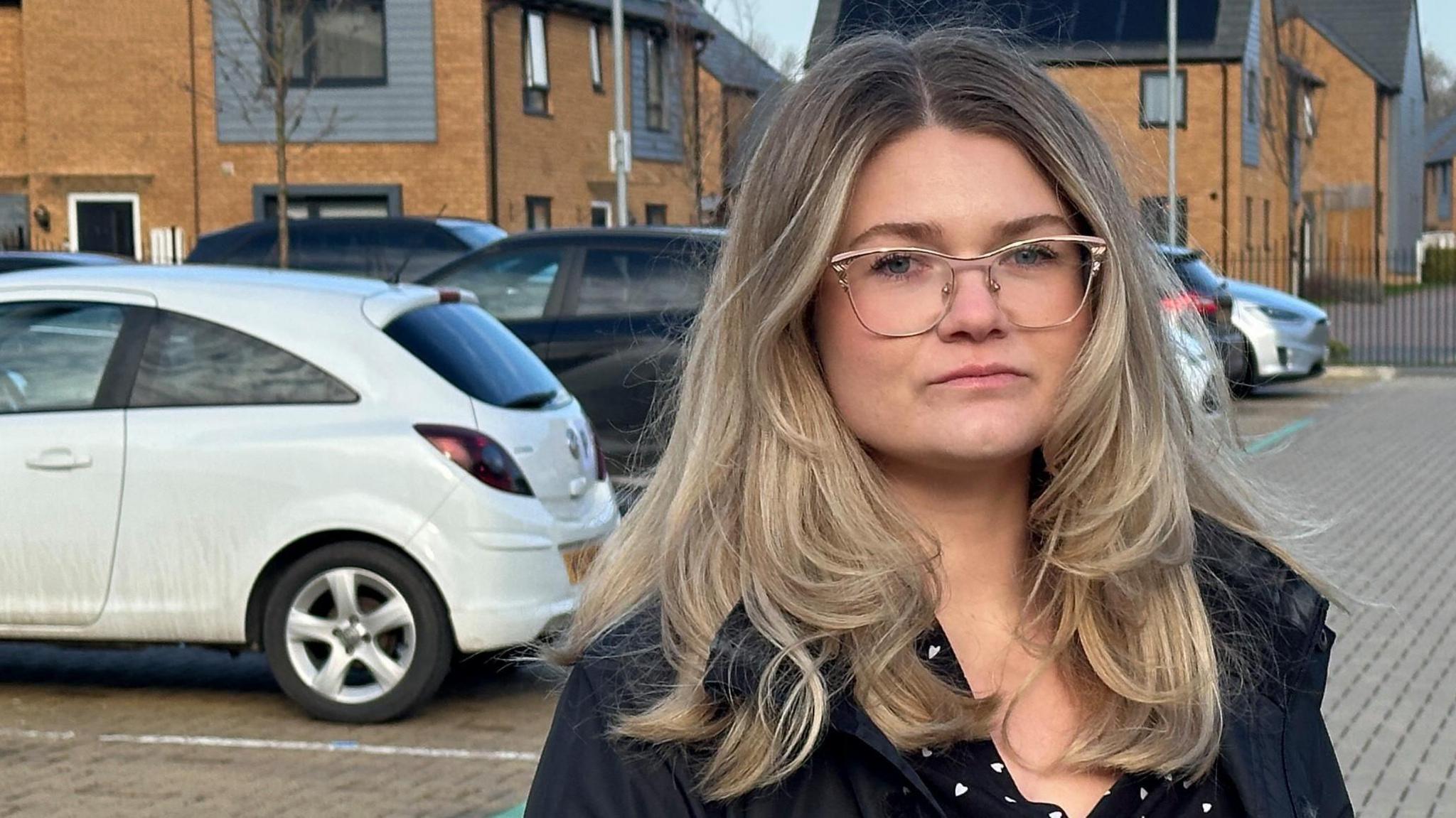 Resident Amy Garrod has long blonde hair and glasses. She is wearing black and stood in a car park on the estate.