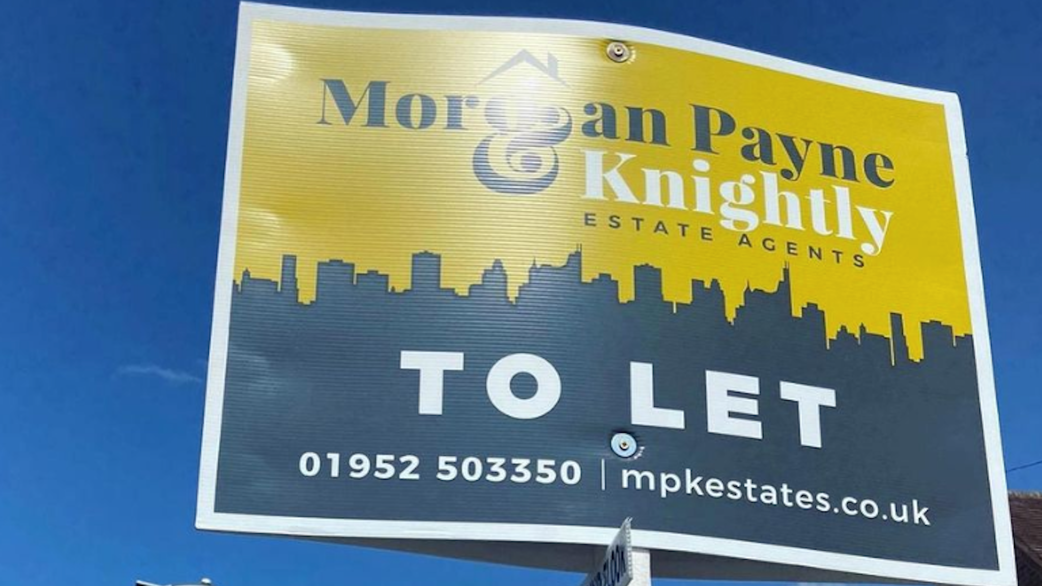 The image shows a sales board for Morgan, Payne & Knightly estate agents against a blue sky
