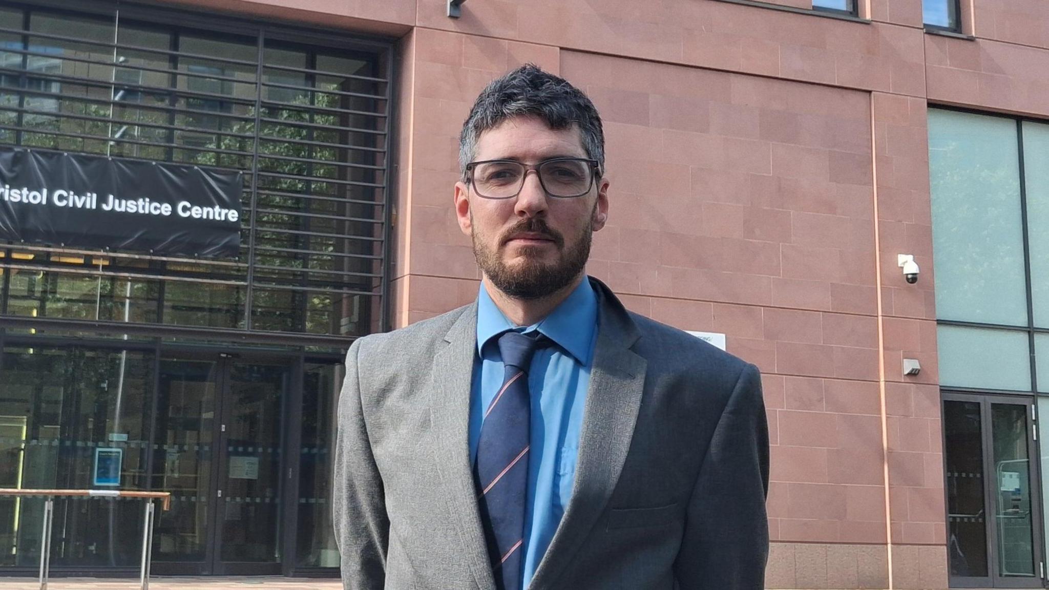 Daniel Adams, who runs Stationery House in Clevedon, outside Bristol Civil Justice Centre where he challenged the parking charges in Clevedon. He is wearing a grey suit, a blue shirt and navy tie.