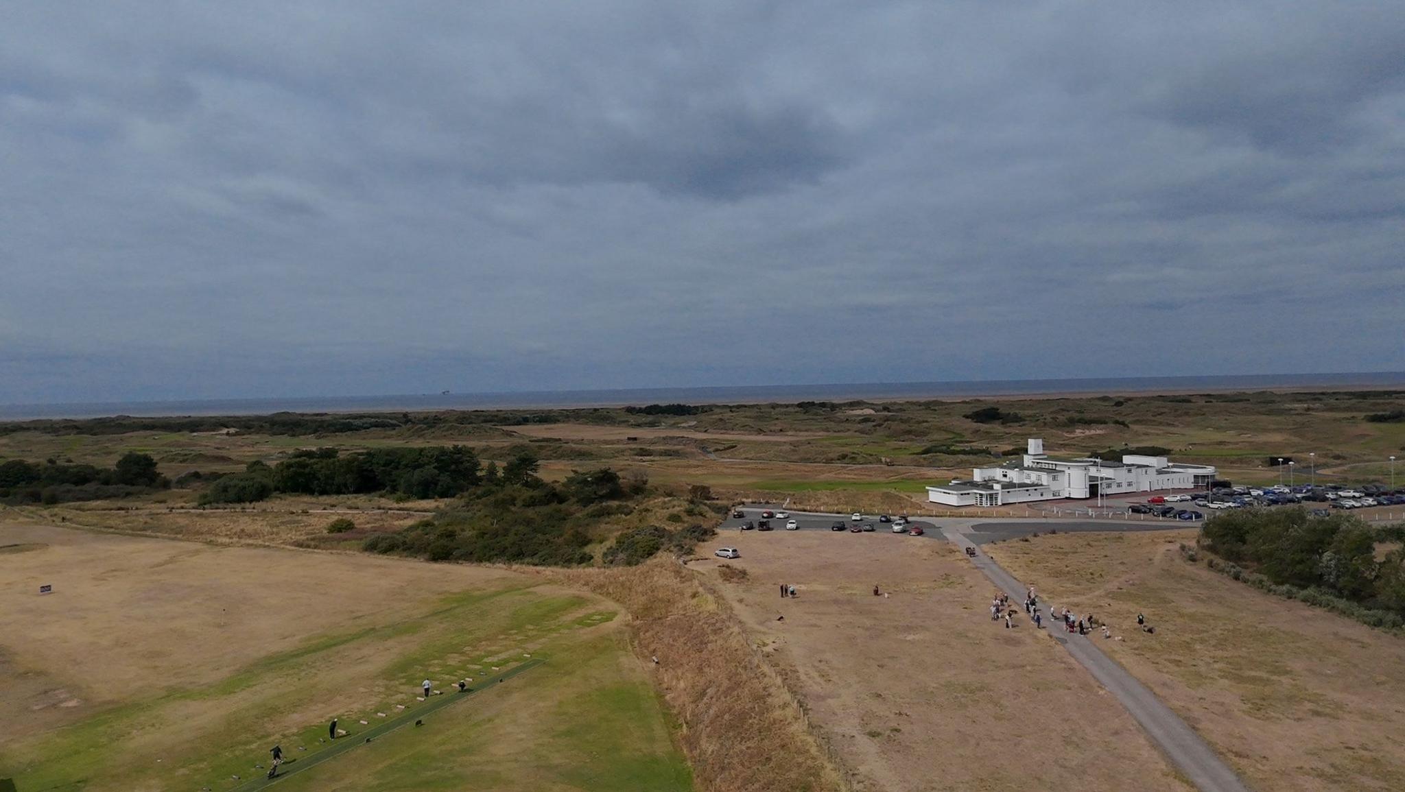 An aerial image shows common land close to Hillside Golf Club. It is a stretch of land behind a band of sand dunes leading down to the beach and the sea beyond. The white Art Deco Royal Birkdale club house is just behind the strip of common land