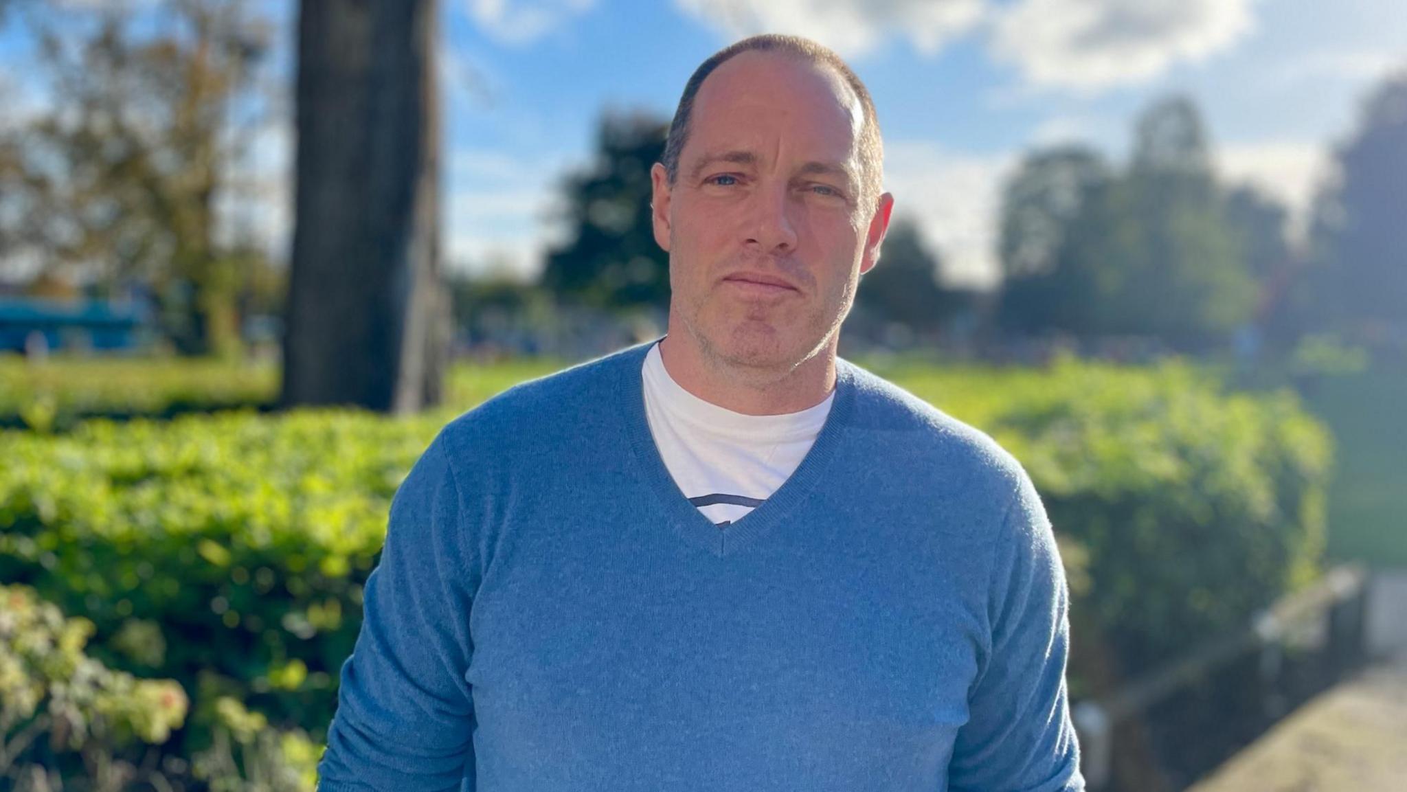 Robert Laycock is wearing a blue jumper and standing outside, he is looking at the camera