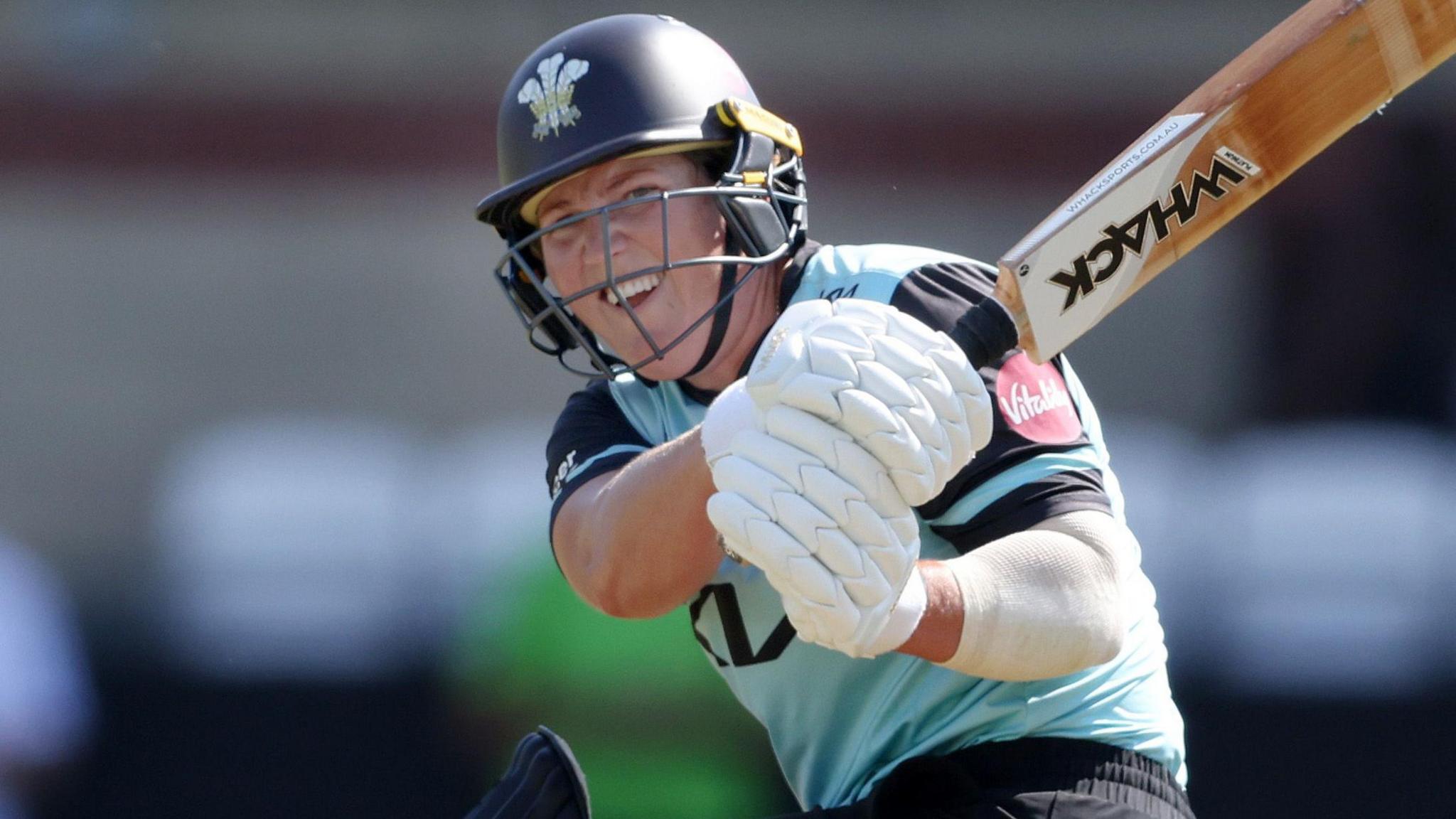 Laura Harris, wearing the Surrey Women's light blue shirt with navy sleeves and navy collar, hits a sweep shot against Warwickshire Bears