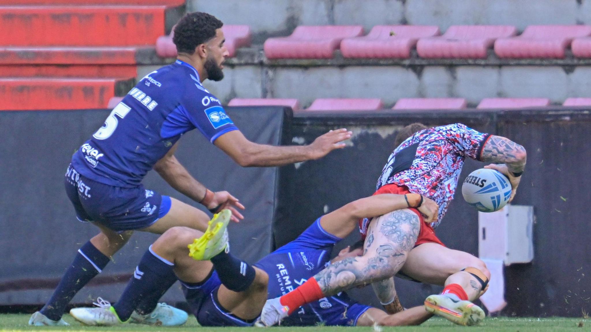 Josh Charnley (CHARNLEY 5) about to score a try on the right with two Toulouse players, one on the floor and one bending down, not being able to stop him