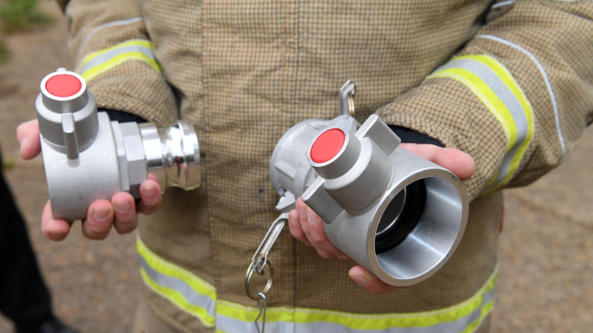 A close-up of two hands holding to specialist adaptors which can connect hoses to water supplies. The person holding them is wearing a firefighter's uniform but you cannot see their face.
