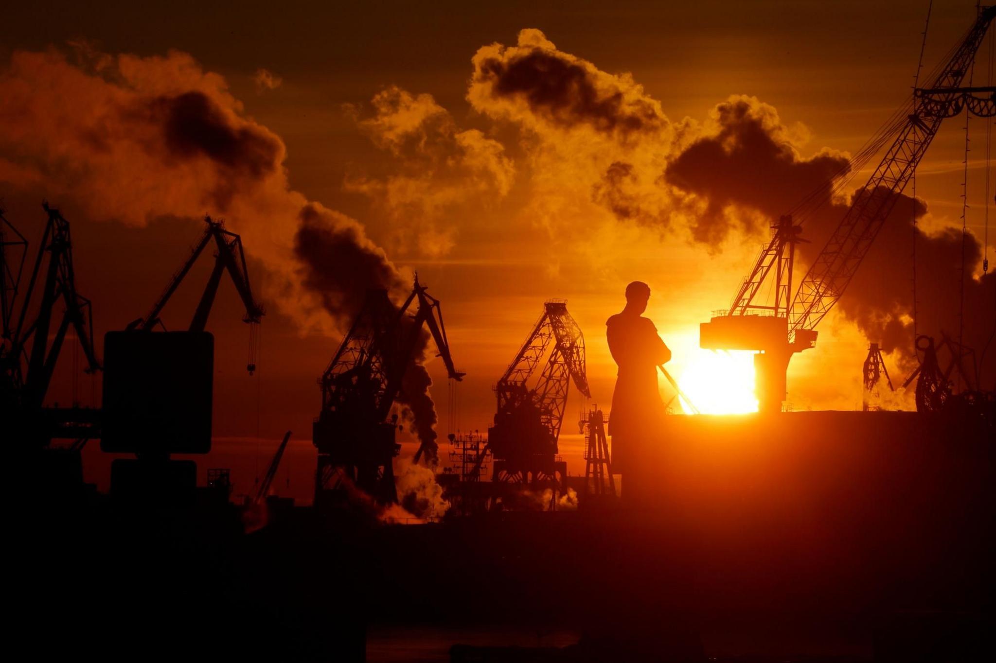 A giant monument to explorer Admiral Ivan Kruzenshtern is silhouetted at sunset in freezing-cold St Petersburg, in Russia. Cranes and clouds are also silhouetted against the orange sky.