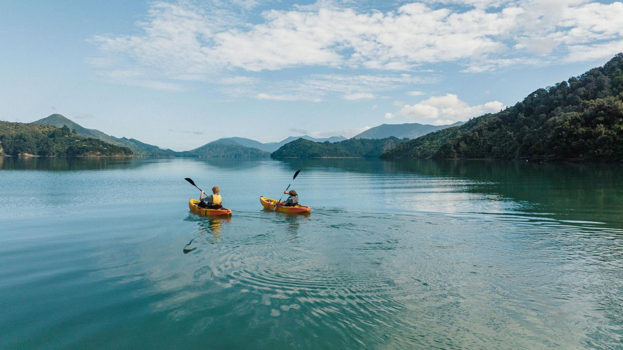 A pair of kayakers on a picturesque lake with mountains in the background