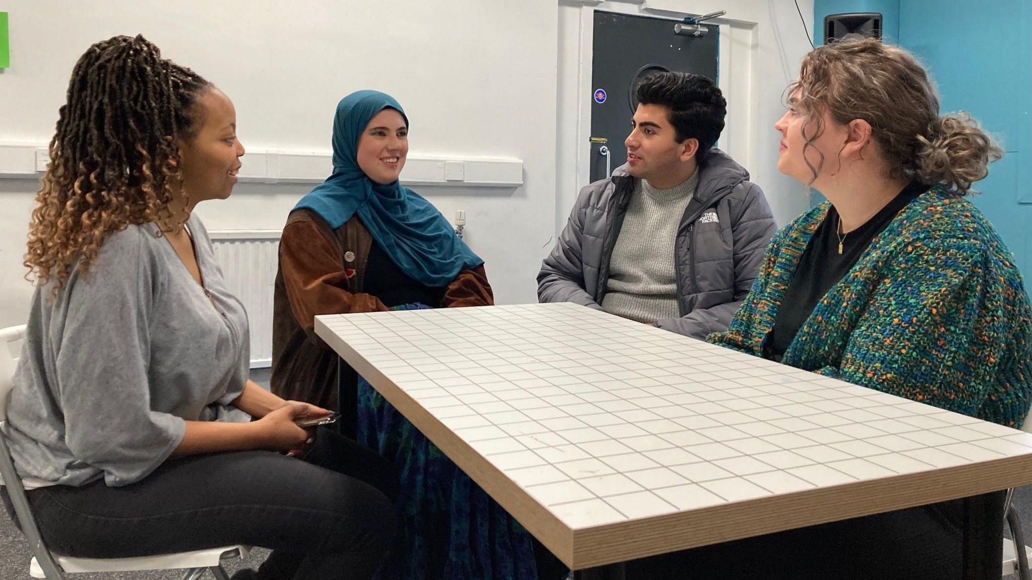 The women and a man sit around a table talking.