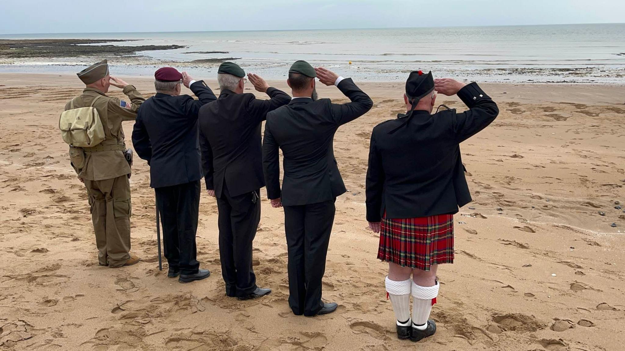 Veterans saluting on the beach looking ahead at the installation of soldiers 