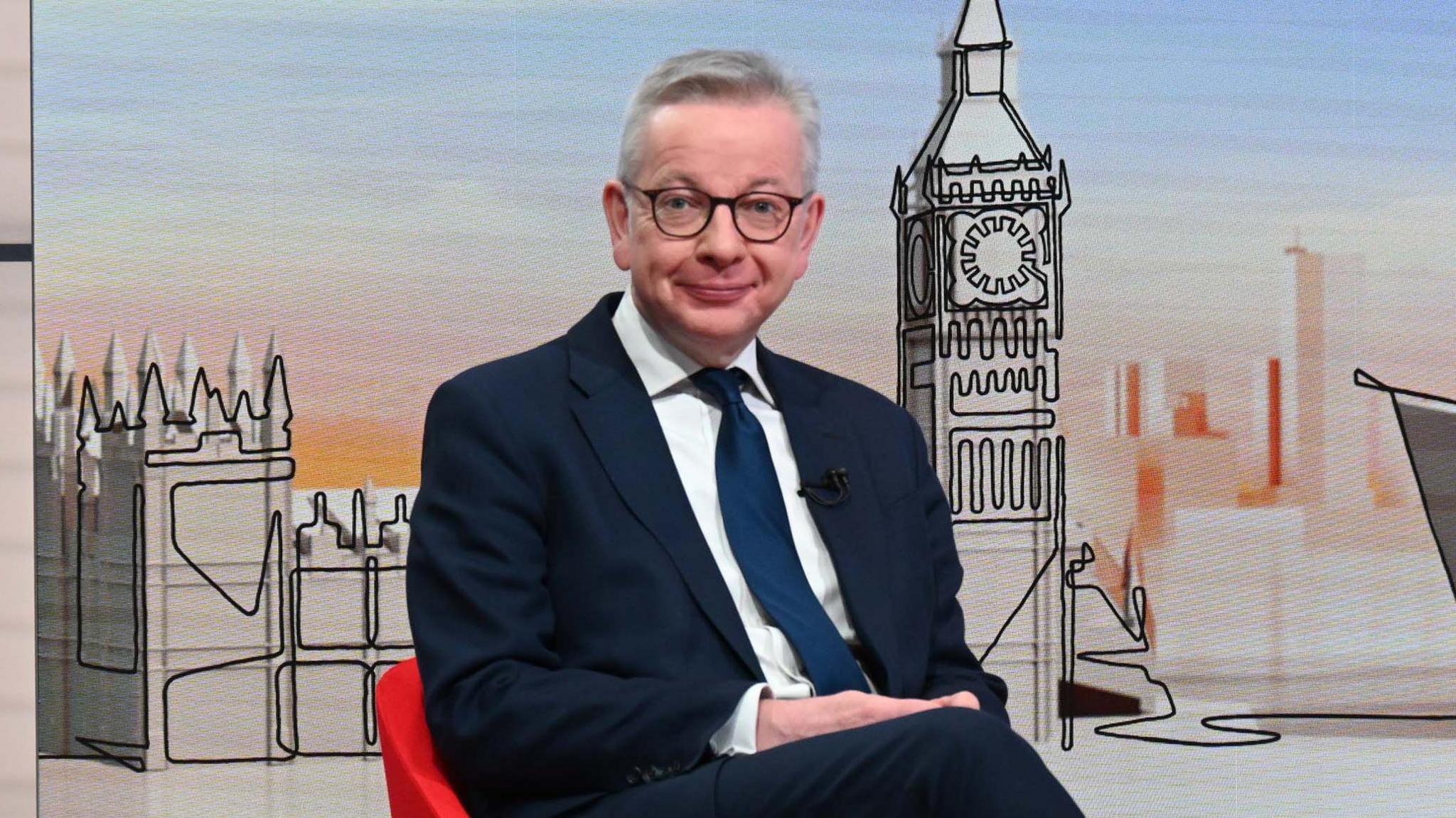 Michael Gove Secretary of State for Levelling Up, Housing and Communities in the TV studio. He is looking at the camera and is wearing a white shirt, navy tie and blazer, plus glasses.