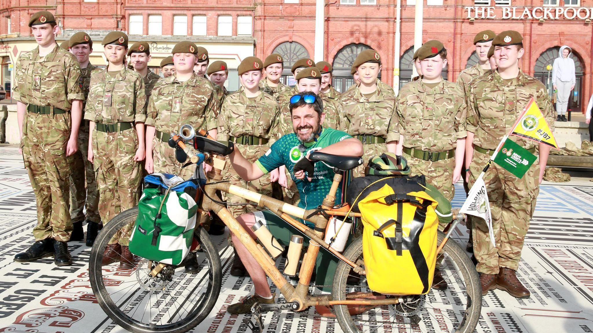 Jordan Wylie poses with a home-made wooden bike on the comedy carpet in Blackpool. Young cadets in army combats stand behind him.