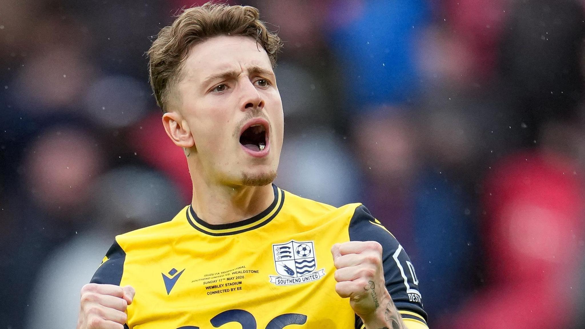 Harry Boyes has his mouth open towards the Southend fans after scoring a penalty at Wembley in the FA Trophy final with Wealdstone. He is wearing a yellow Southend away kit.