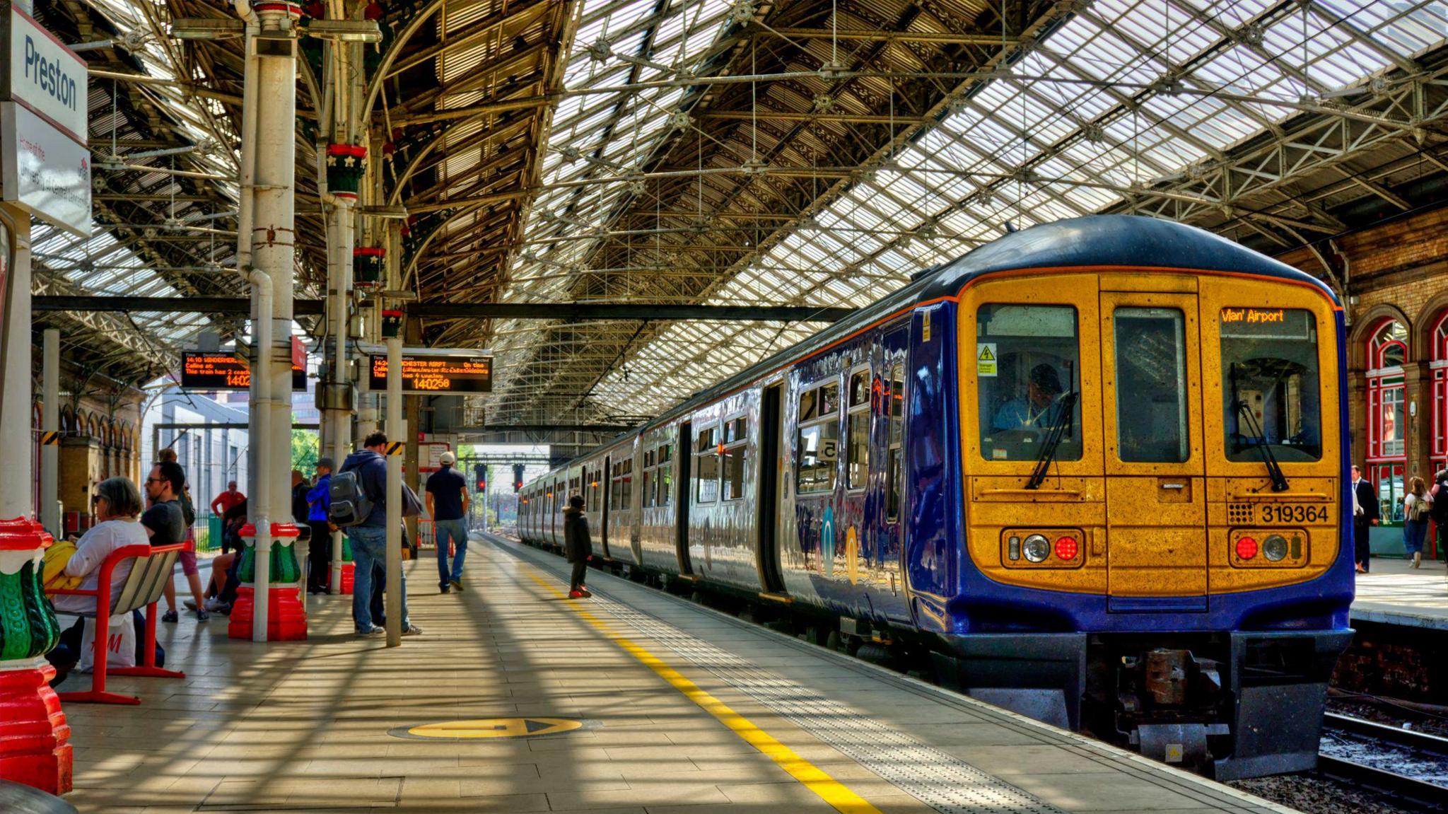 Stock image of a blue train with a yellow front. It stands at a Preston railway station platform.