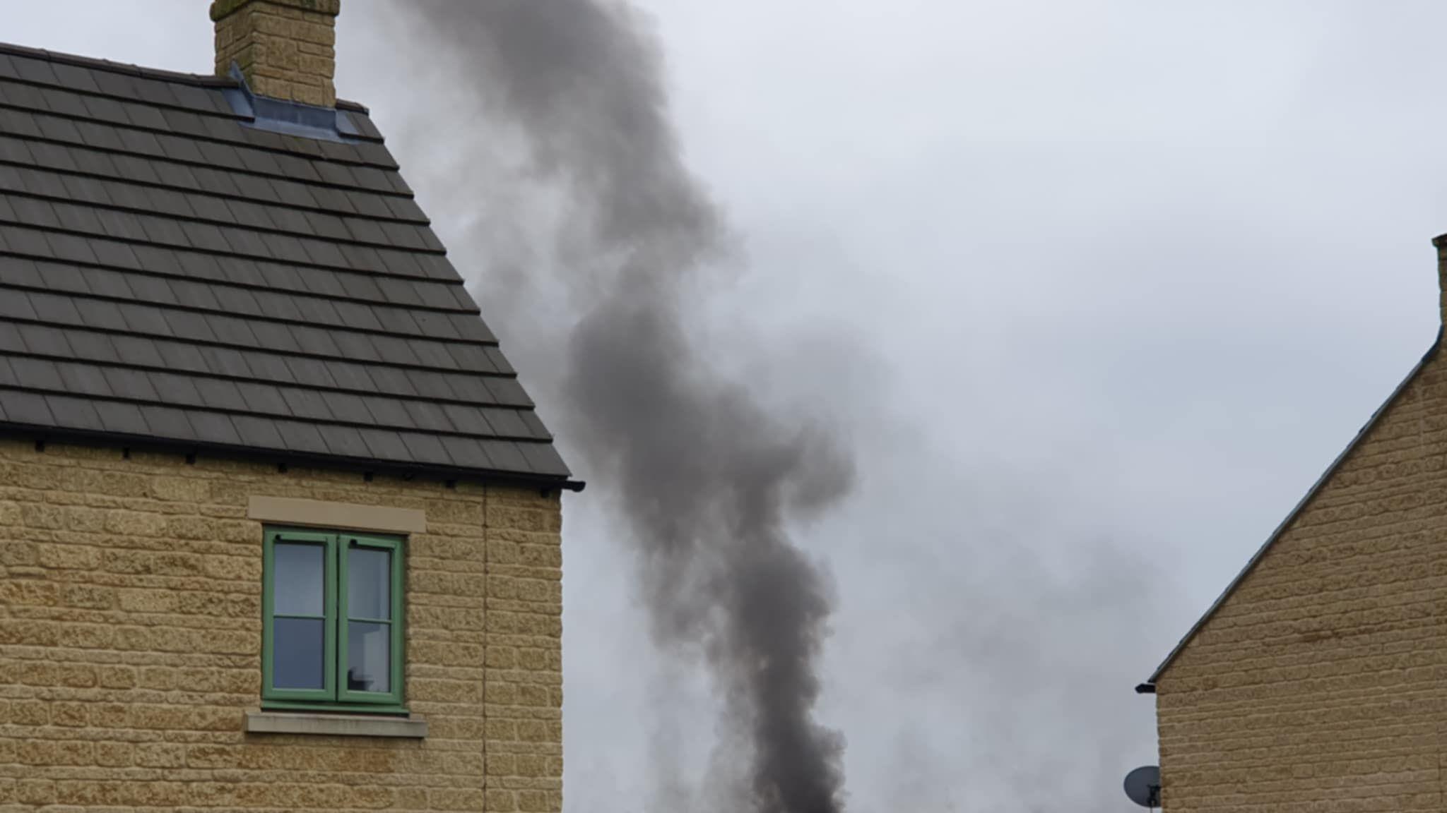 A thick plume of black smoke pictured next to a house