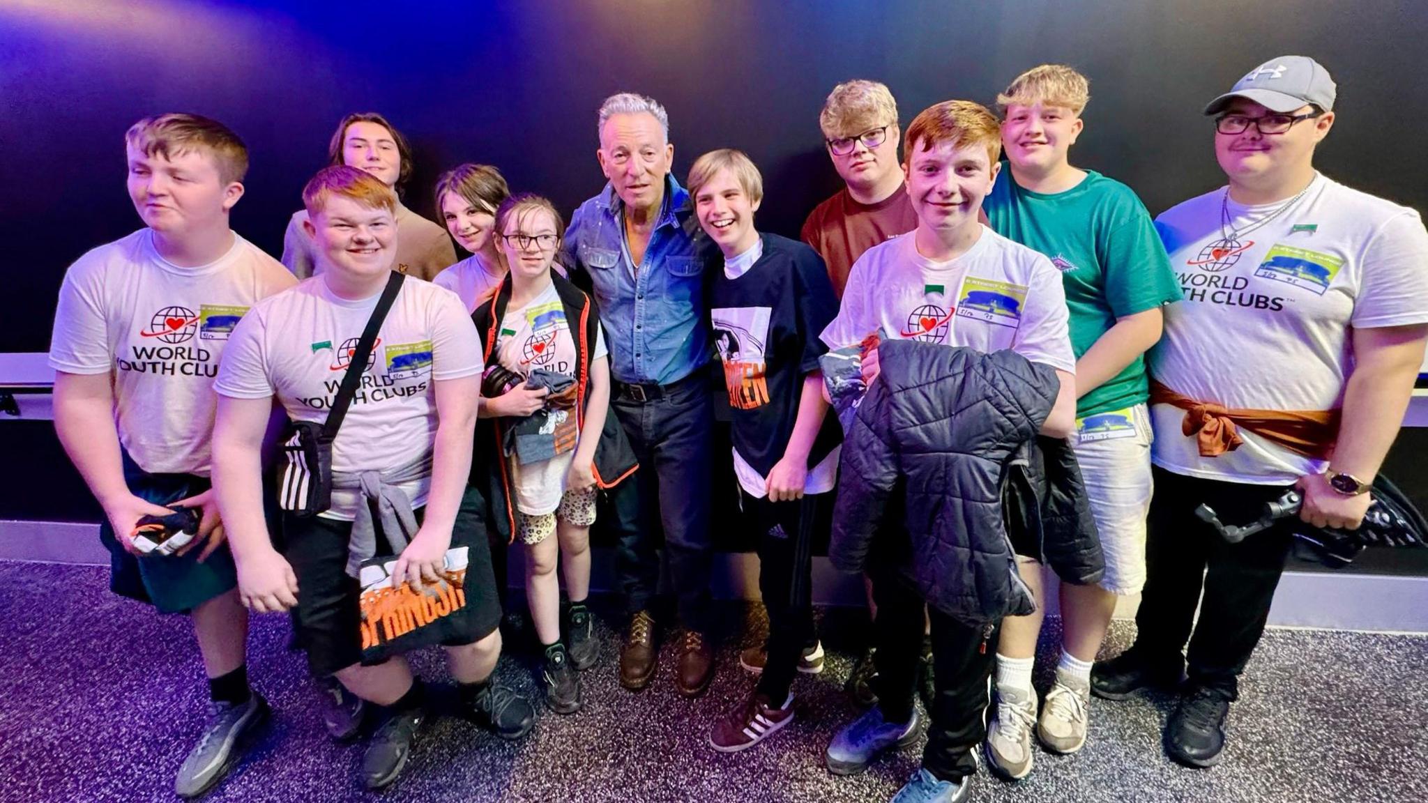 A group of ten teenagers stand smiling with Bruce Springsteen.