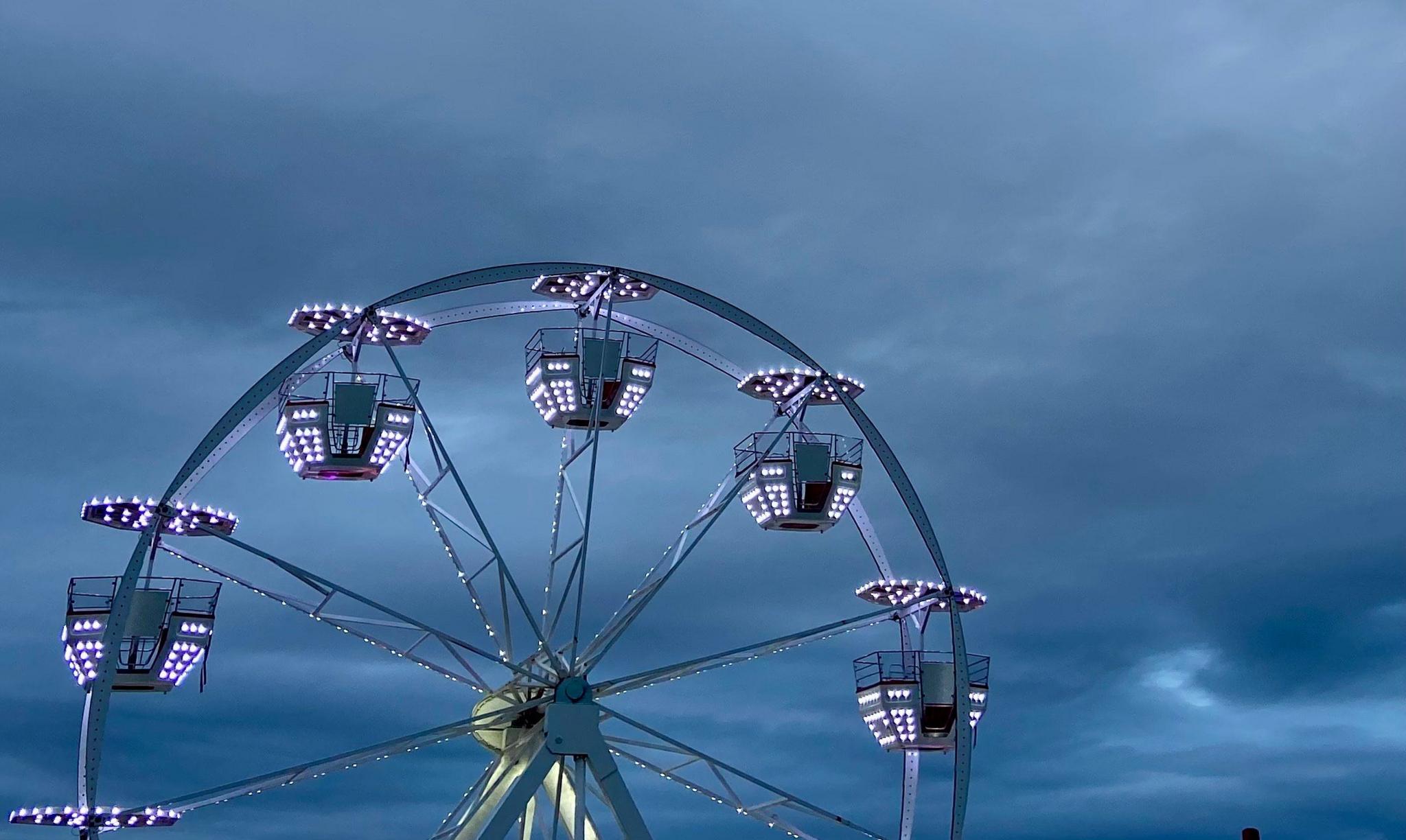 Top half of a lit up Ferris wheel against a dark grey cloudy sky