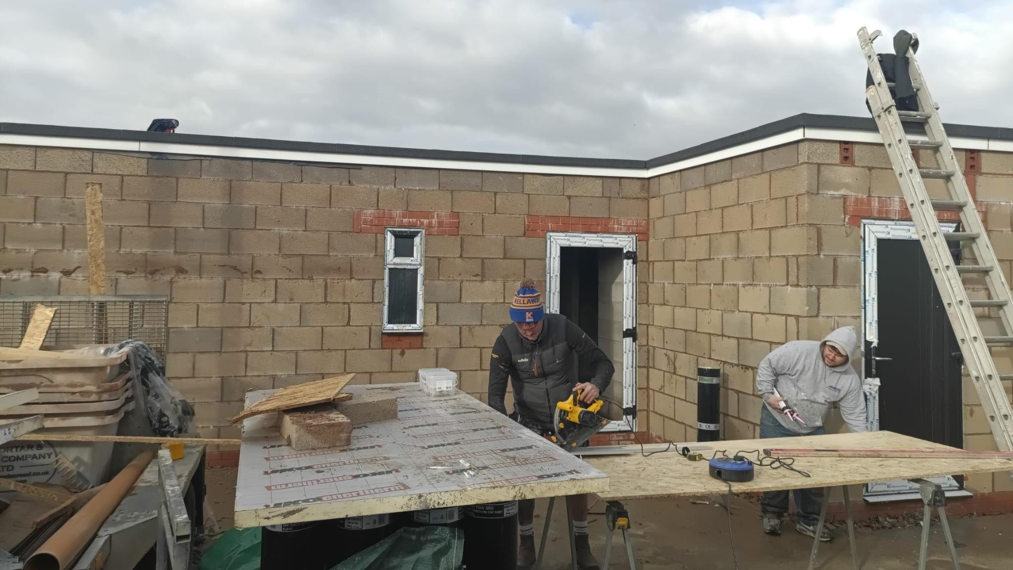 Two men with drills  are working on building a new changing room bloxk in Warwick