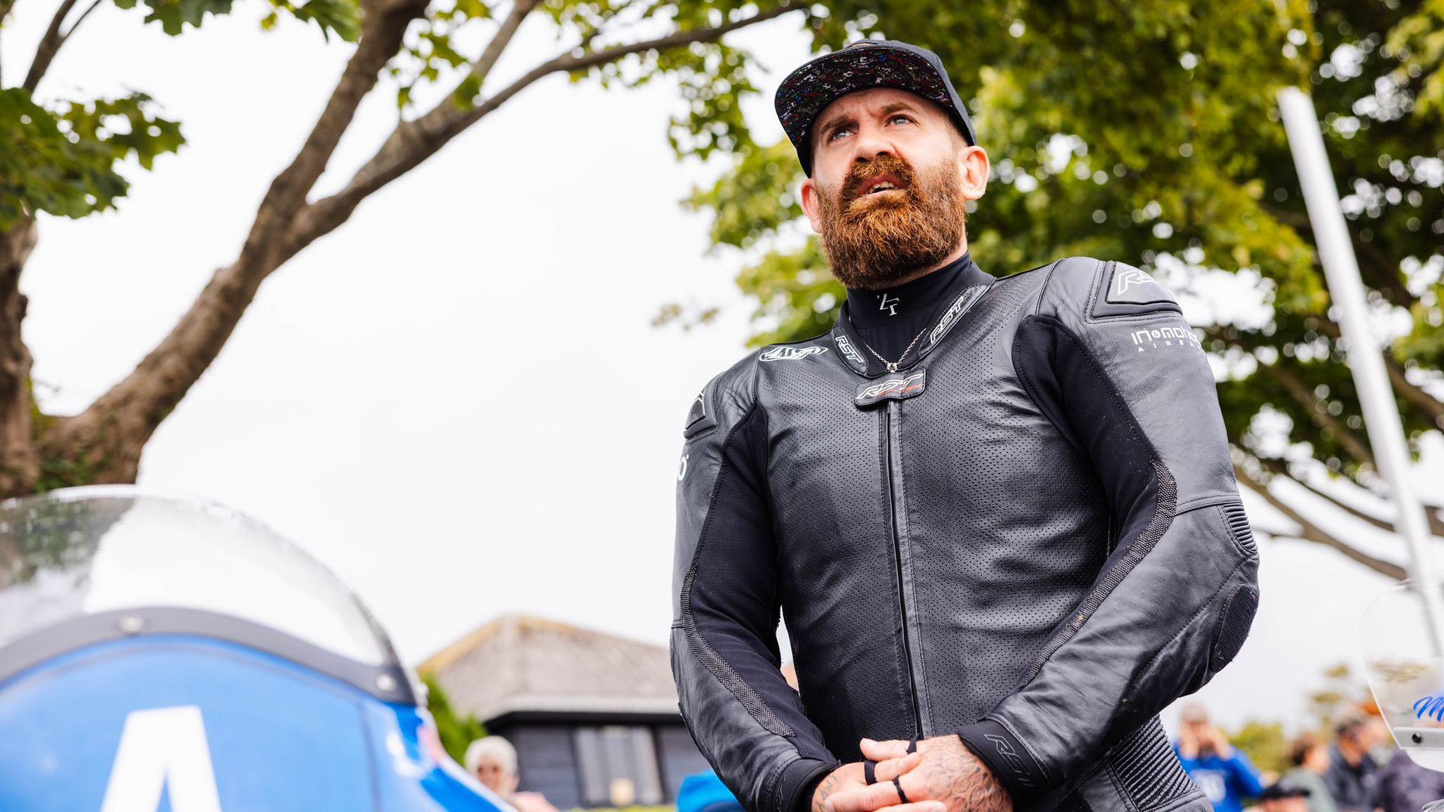 Jamie Coward, who has a beard and is wearing a cap and black leathers, standing next to his bike.
