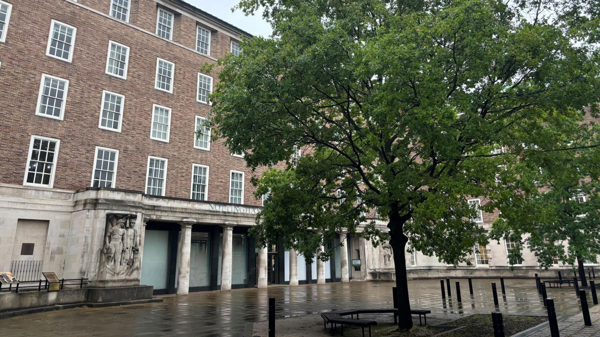 Nottinghamshire County Hall in West Bridgford, with a tree in front of it. It is a tall brick building with many windows and two trees in front of it