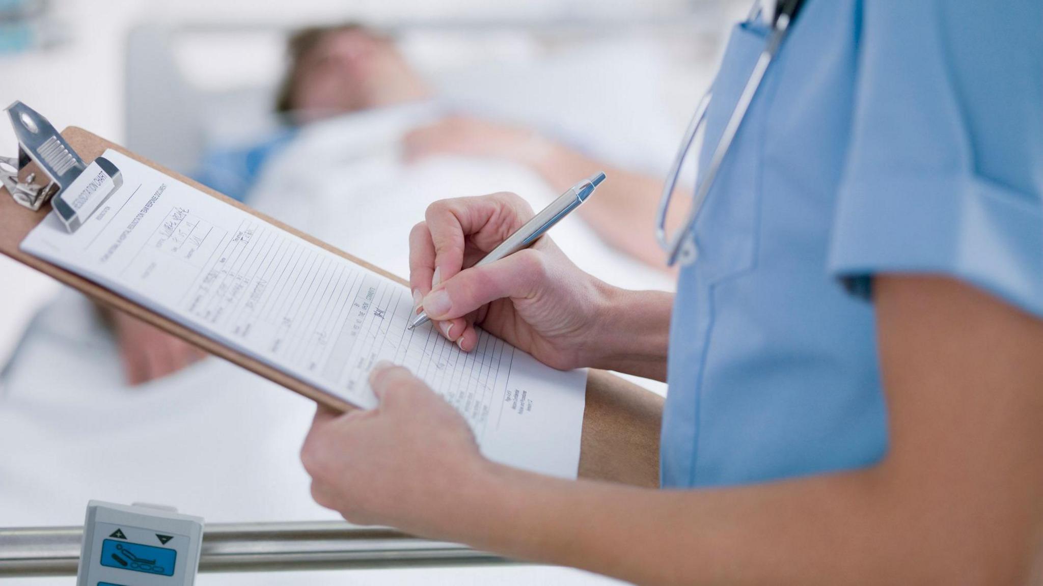 nurse with chart standing next to hospital bed