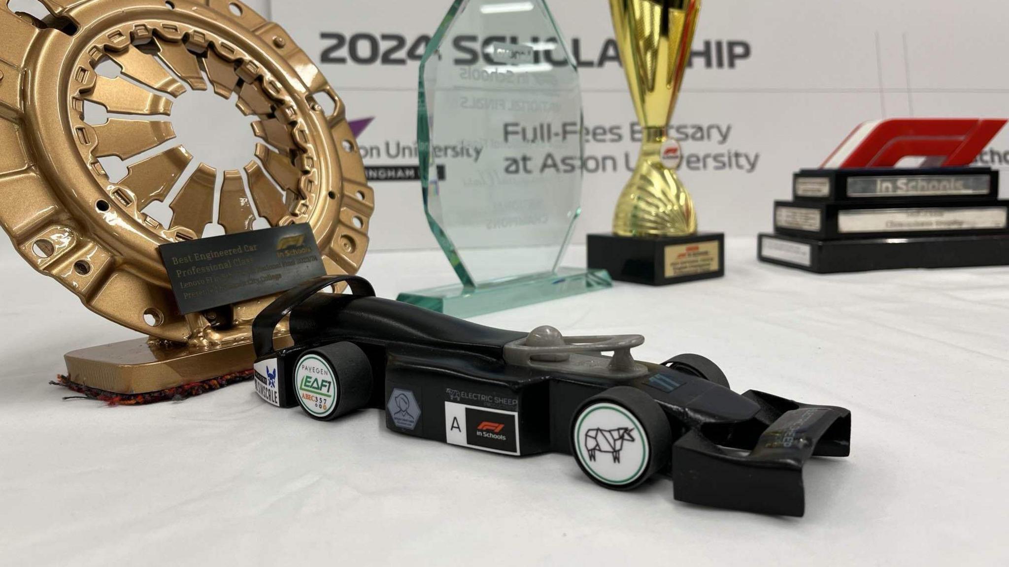 A black model Formula 1 car on a white cloth with trophies behind