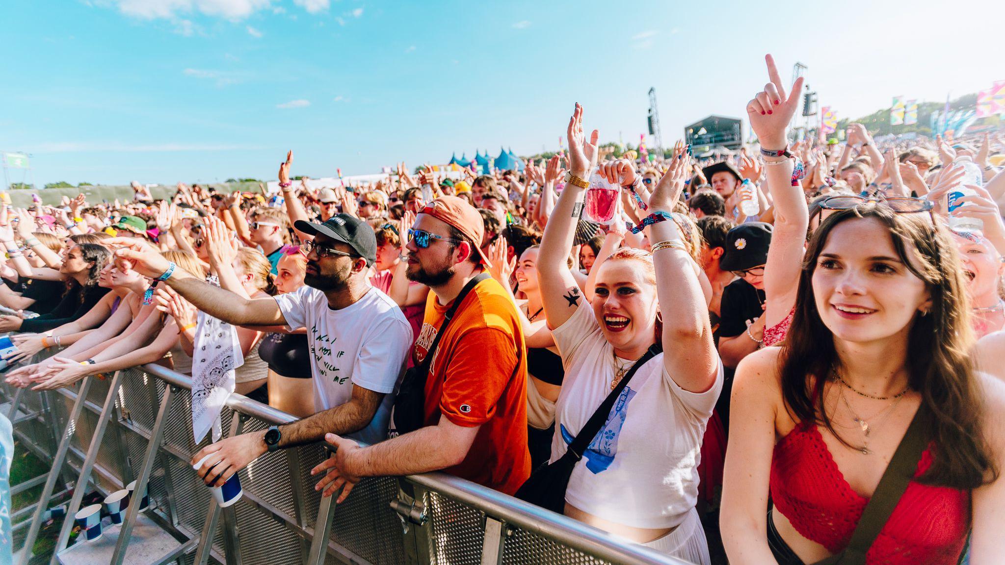 The crowd at Truck festival up against a metal barrier. The sky is blue.