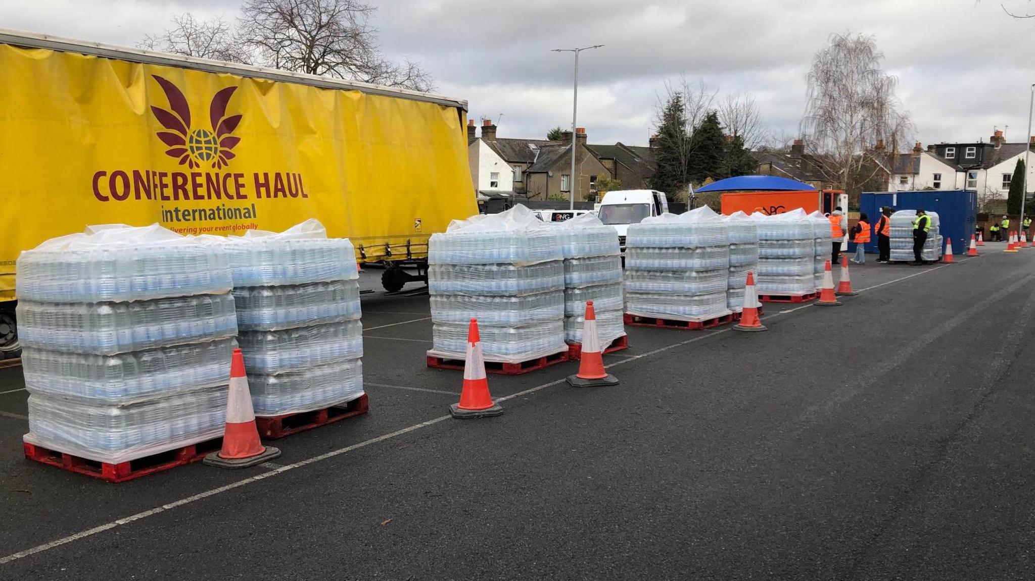 Crates of bottled water are lined up in front of a yellow lorry