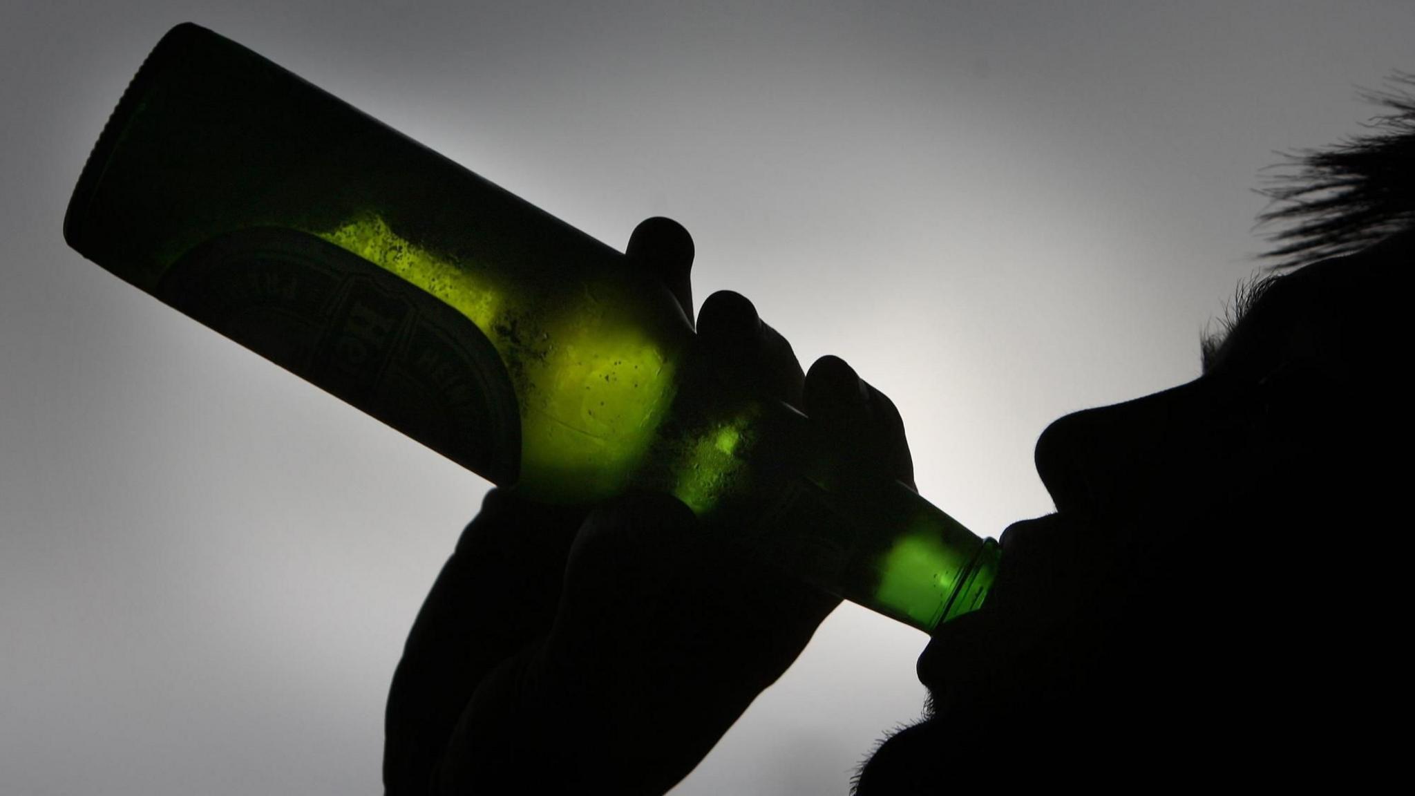 Green bottle being tilted into someone's silhouetted mouth