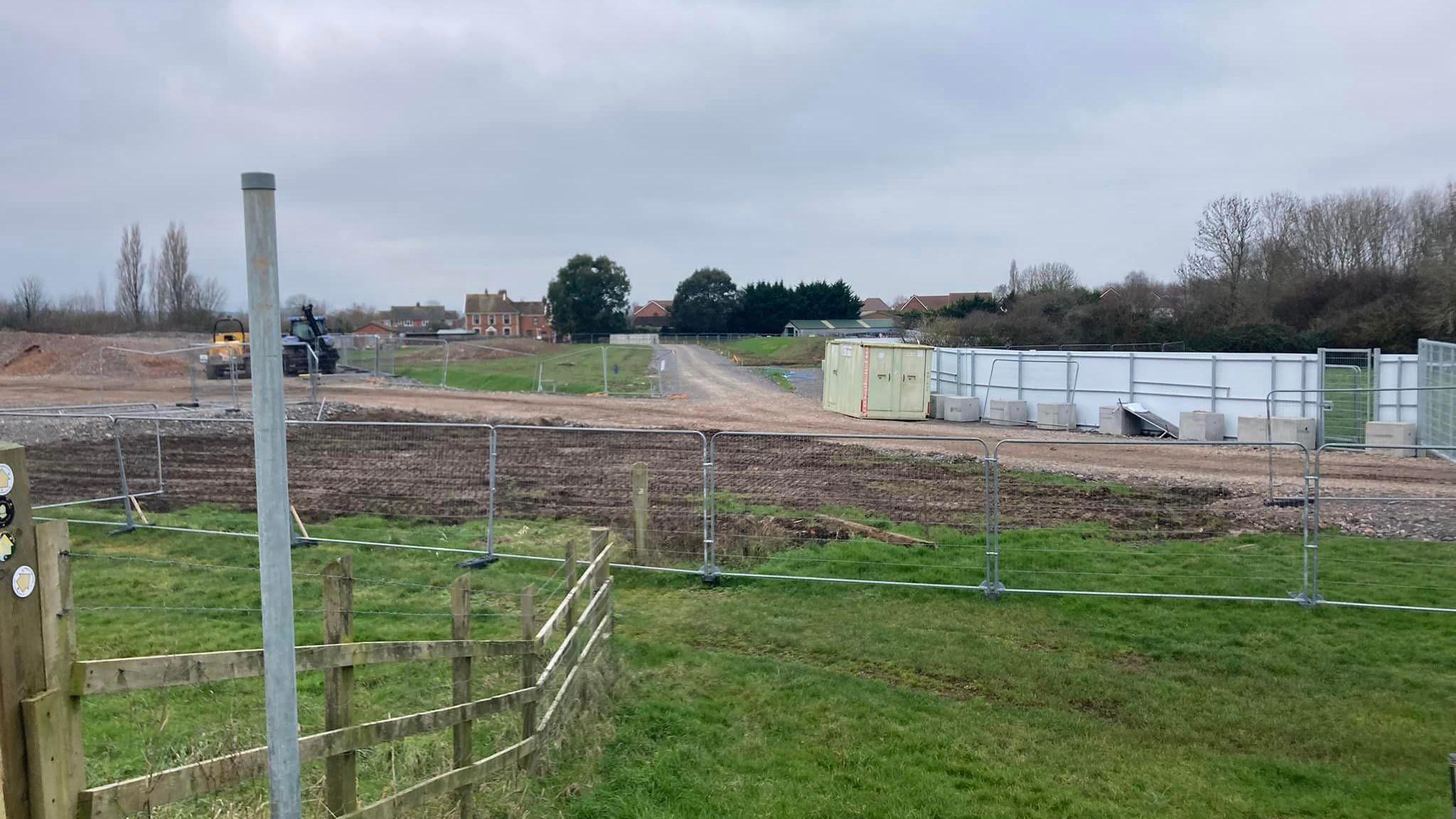 a building site of muddy fields and diggers with a fence around it